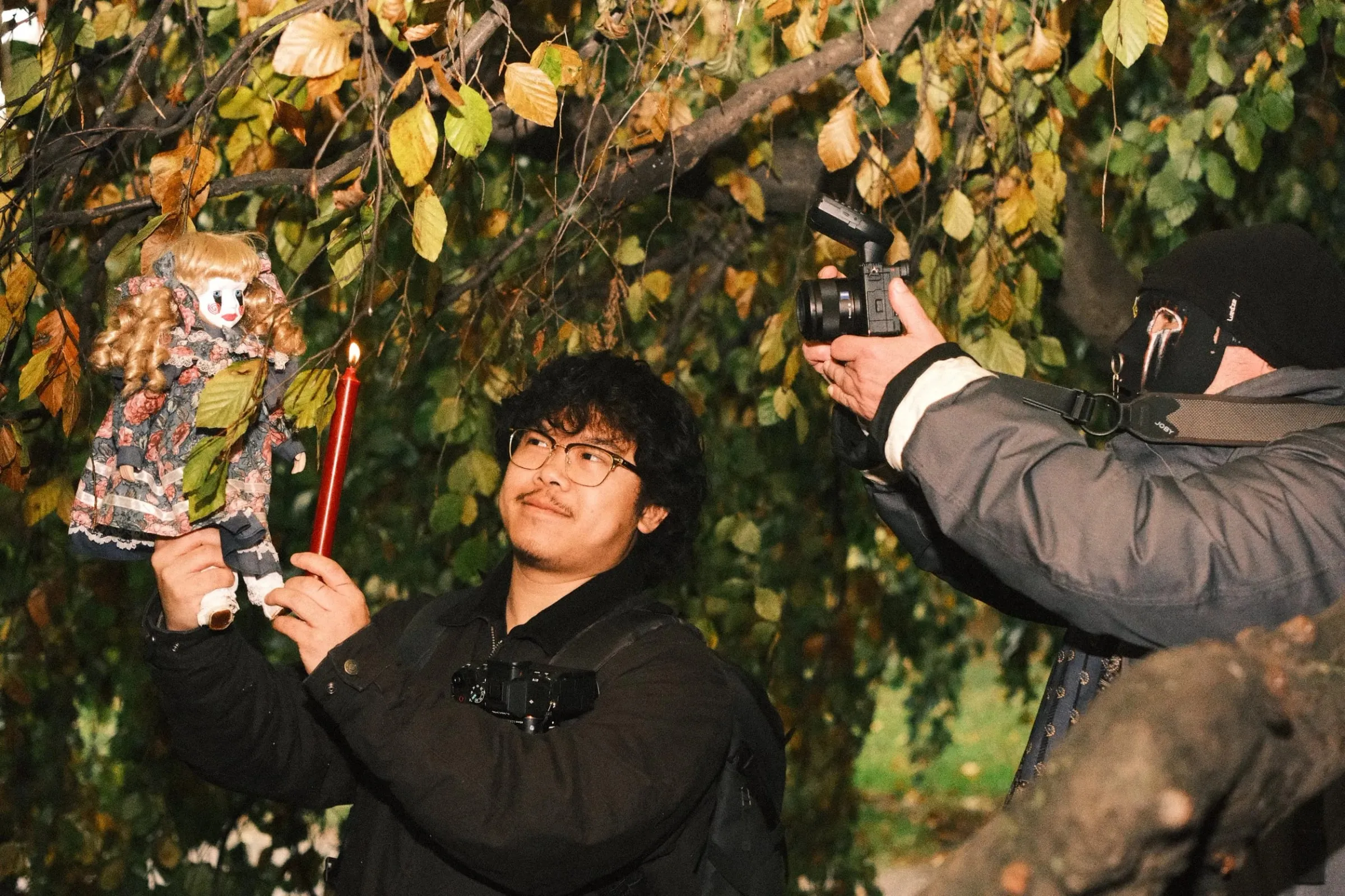 A photographer holding up an old doll and a red candle while others take photos in the trees