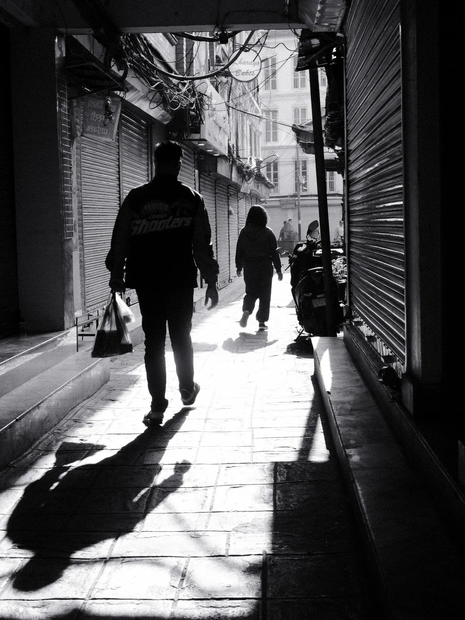 Black and white photo of people walking down a sunlit lane, with long shadows
