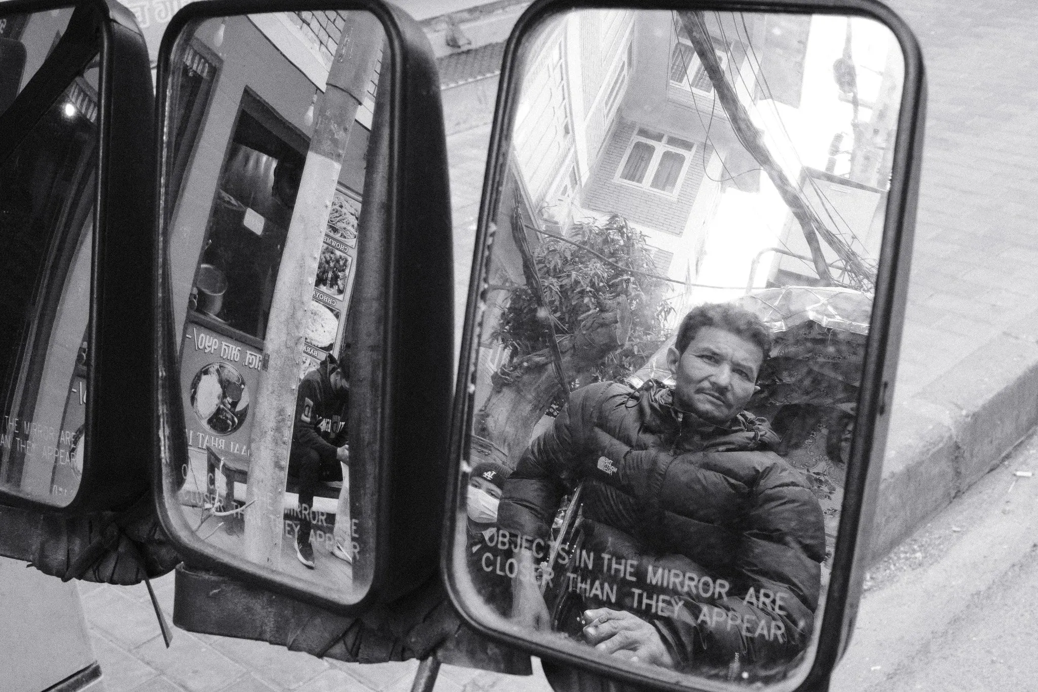 Black and white photo of a man reflected in a pair of vehicle mirrors