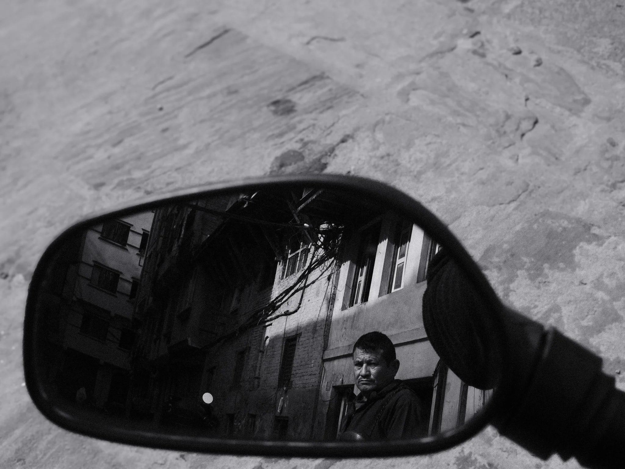 Black and white photo of a man reflected in a motorbike wing mirror in Kathmandu