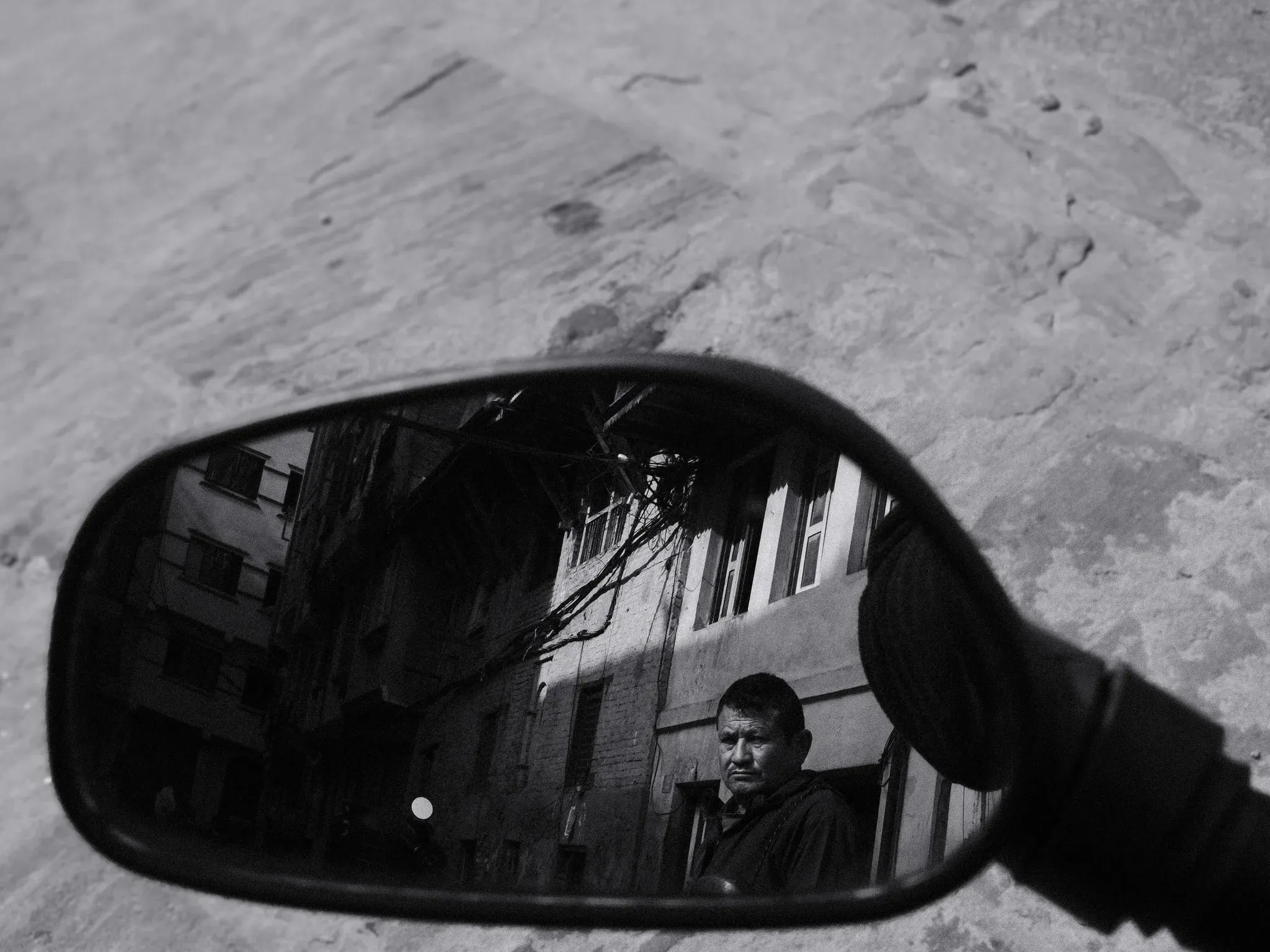 Black and white photo of a man reflected in a motorbike wing mirror in Kathmandu