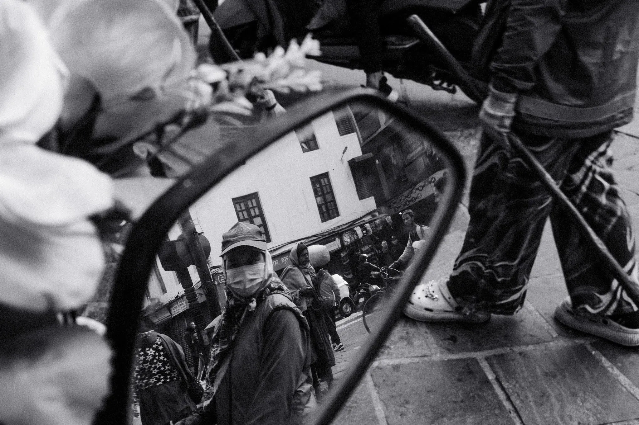 Black and white photo of a masked man reflected in a mirror on a busy street