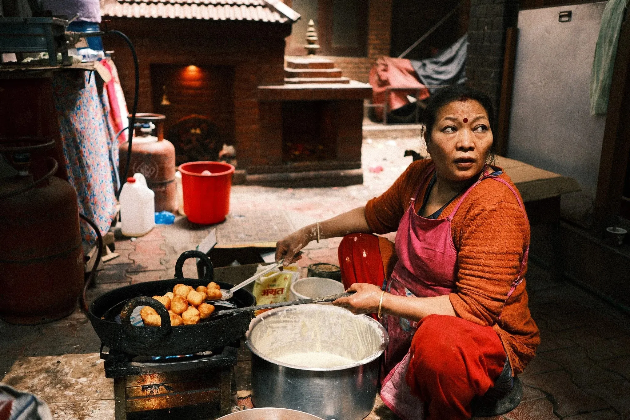 A woman frying dough balls in a pan in a courtyard