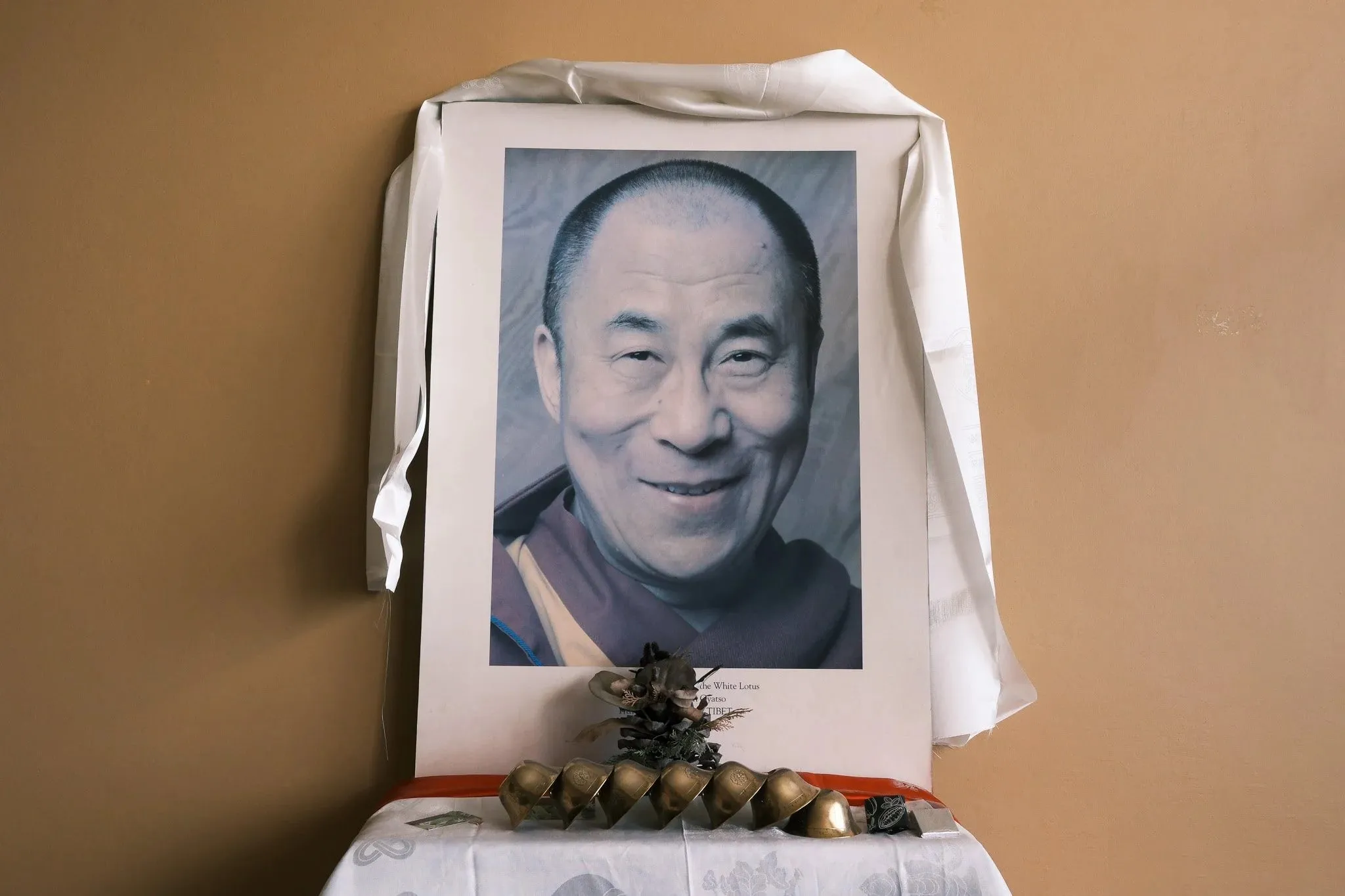 A framed portrait of the Dalai Lama draped with a white scarf on an altar