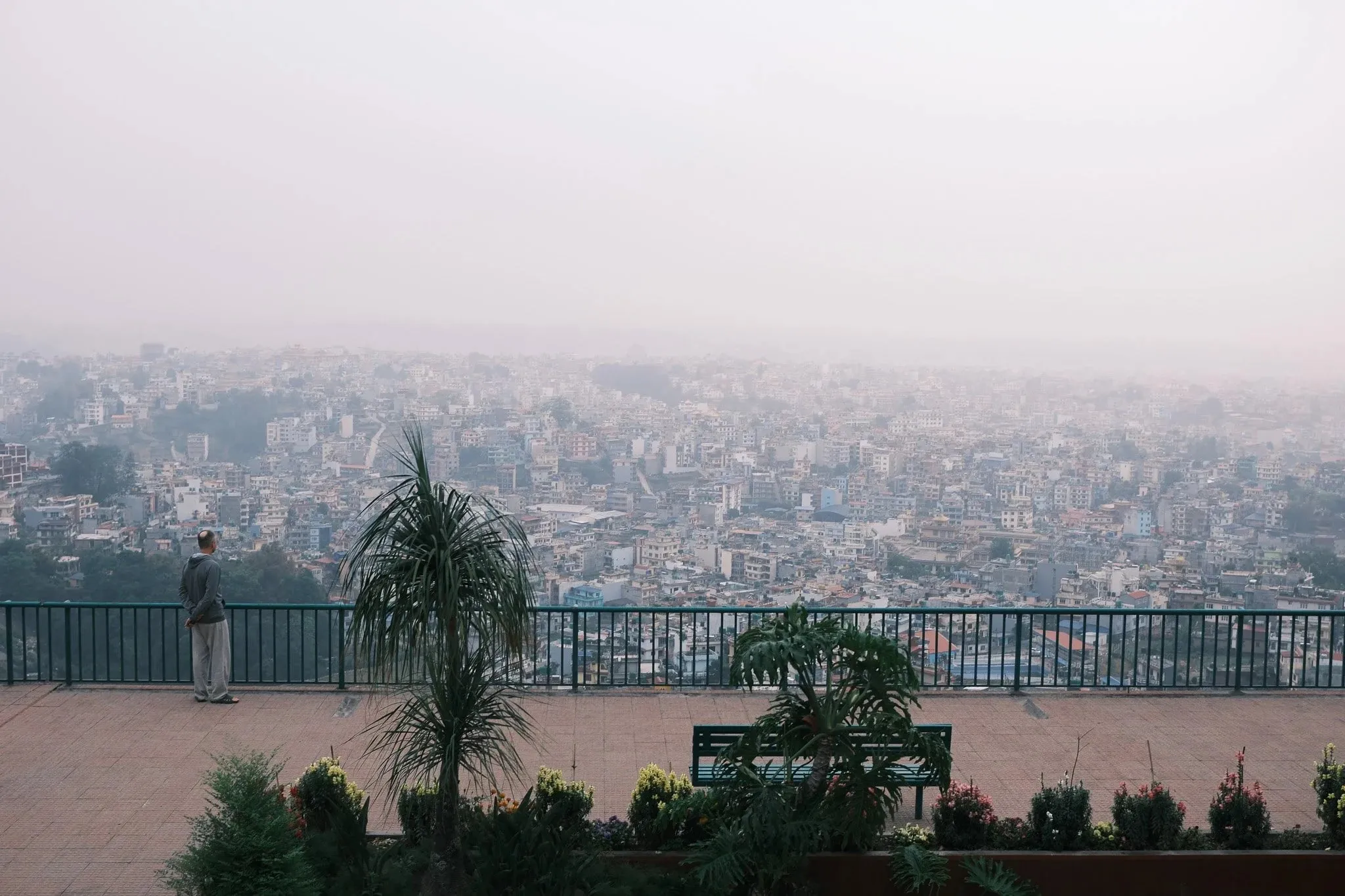 A person at a railing looking out over hazy Kathmandu from the hilltop at Kopan