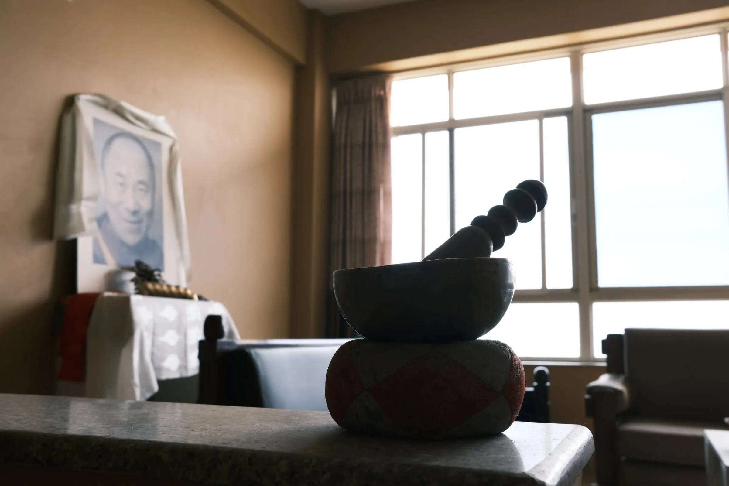 A singing bowl on a cushion by the window of a room at Kopan Monastery, with a framed portrait behind