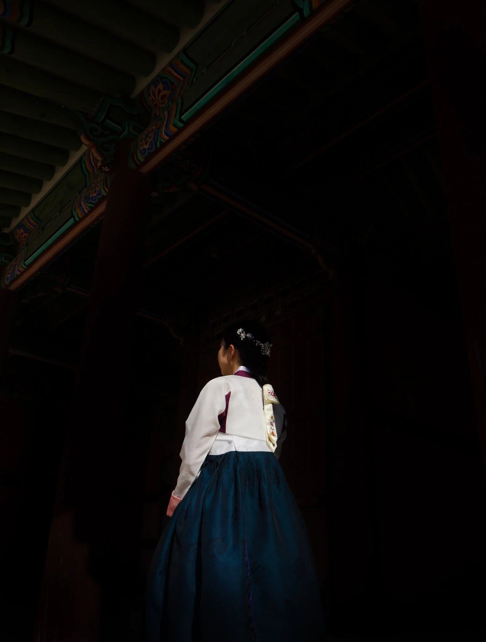 Woman in hanbok seen from behind, standing in a dark doorway