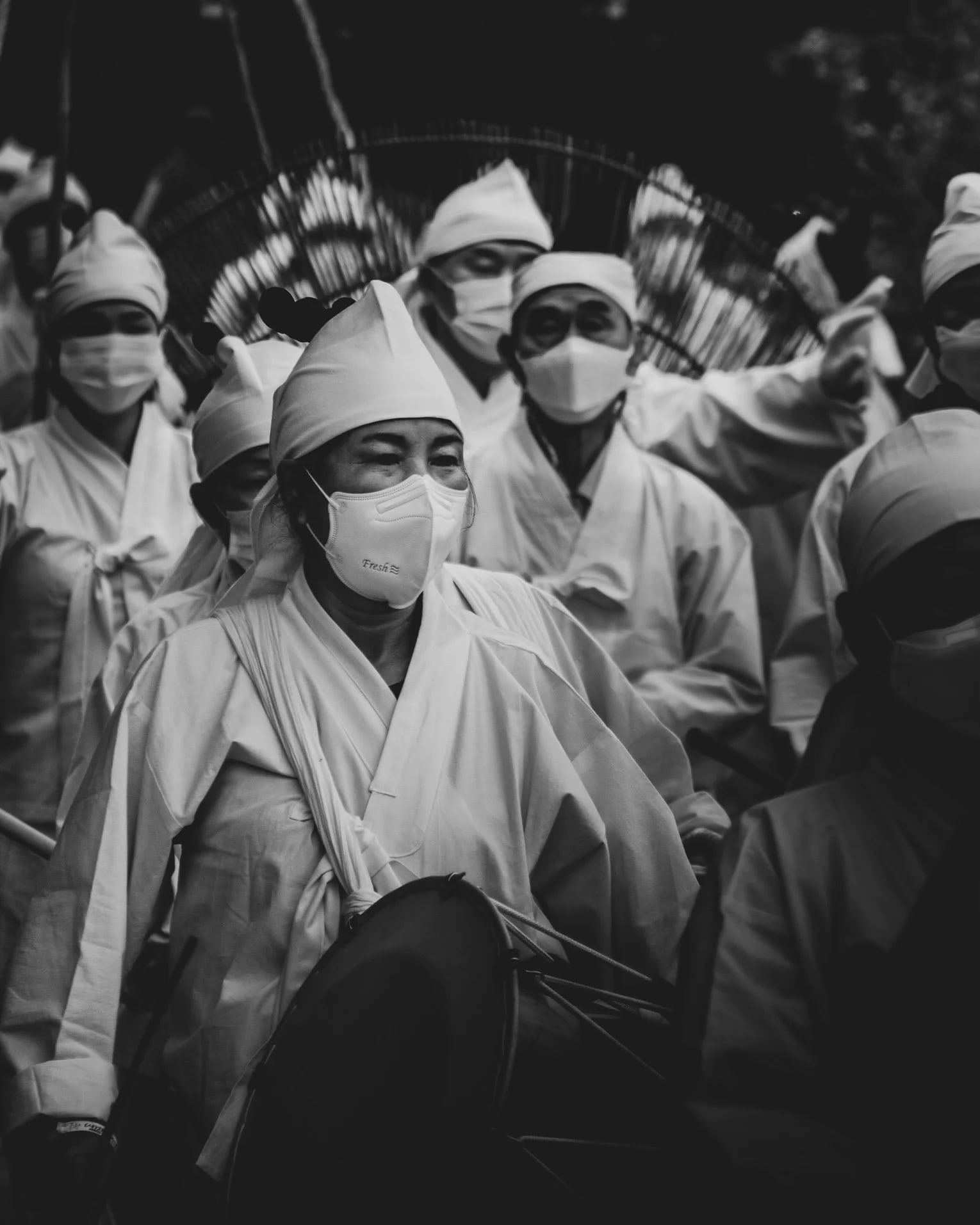 Crowd in white traditional dress and pointed hats at a procession, in black and white