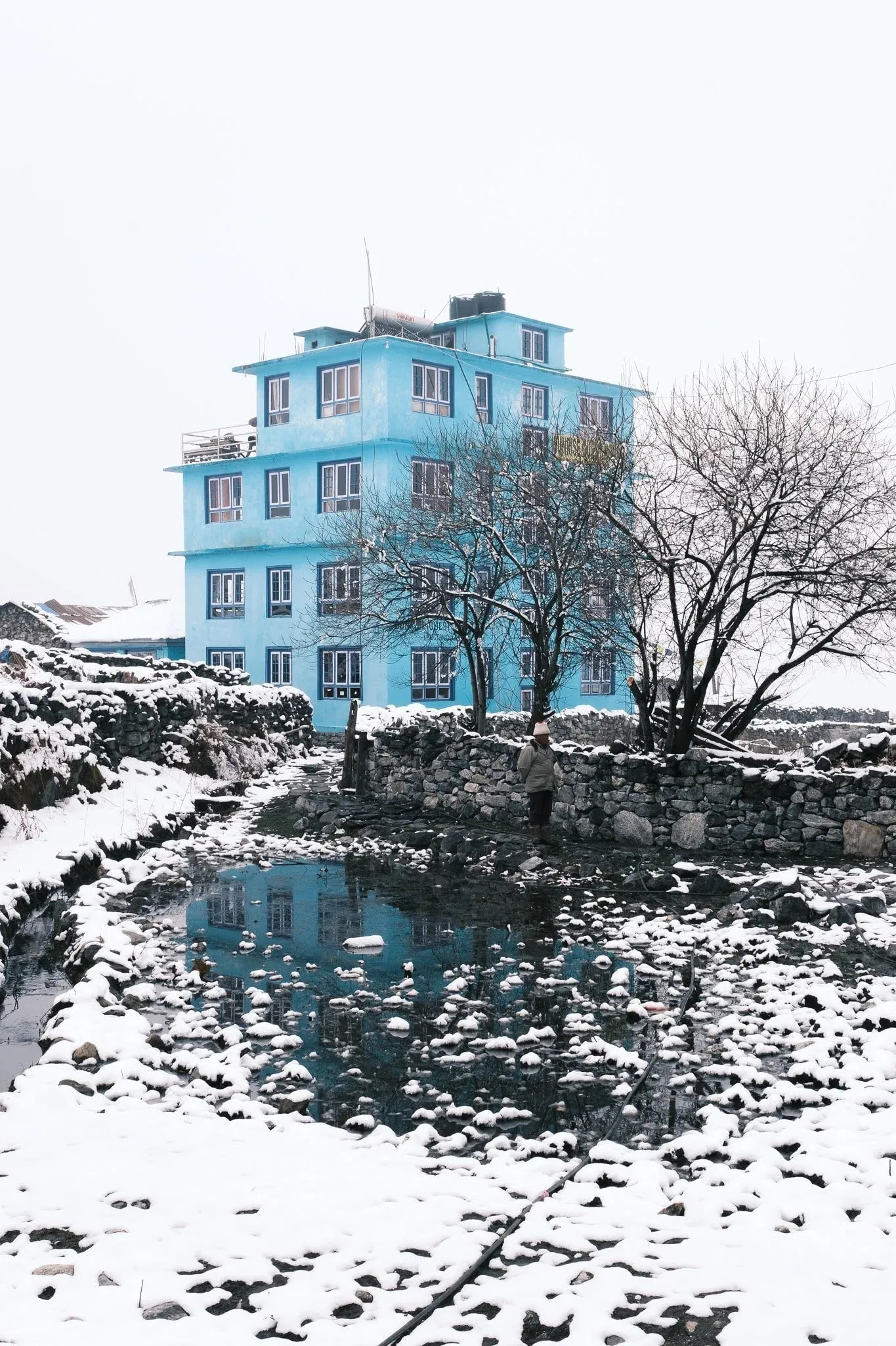 A bright blue lodge behind a pond and stone walls in the snow