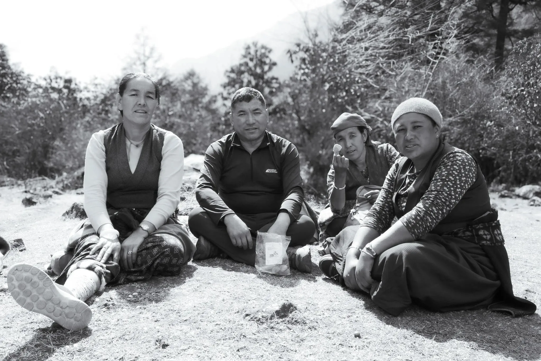 Black and white photo of four people sitting together on the ground by the trail