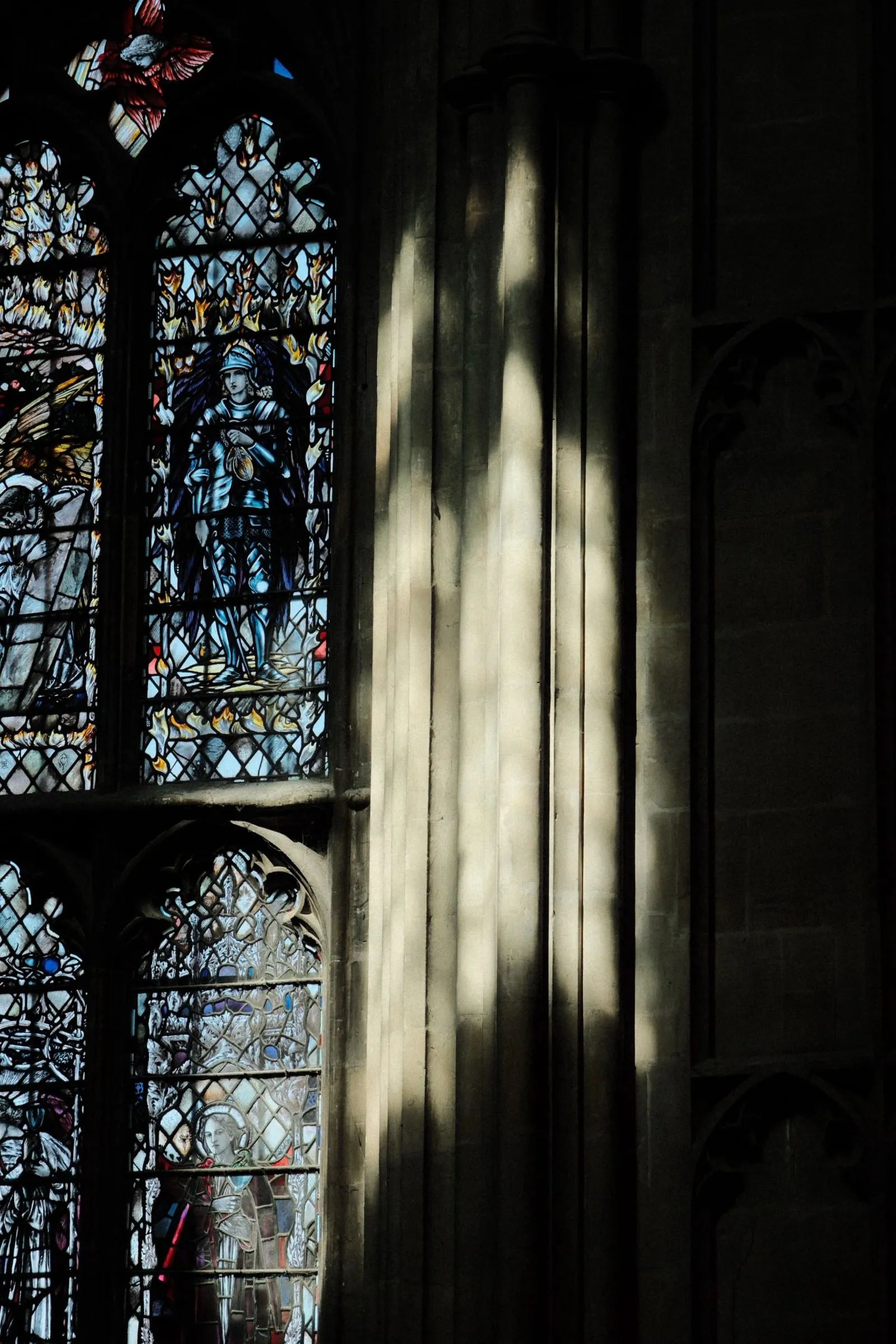 Sunlight striping a stone pillar in front of stained glass windows