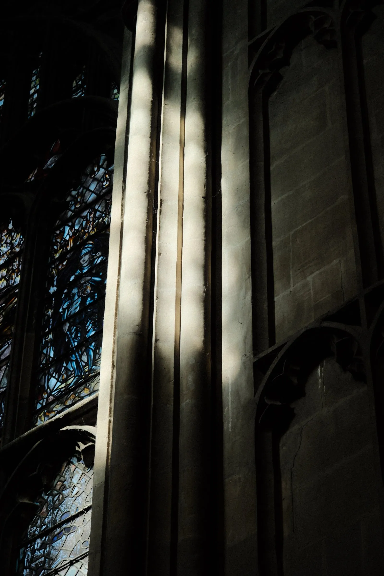 Bands of light across clustered stone columns beside stained glass