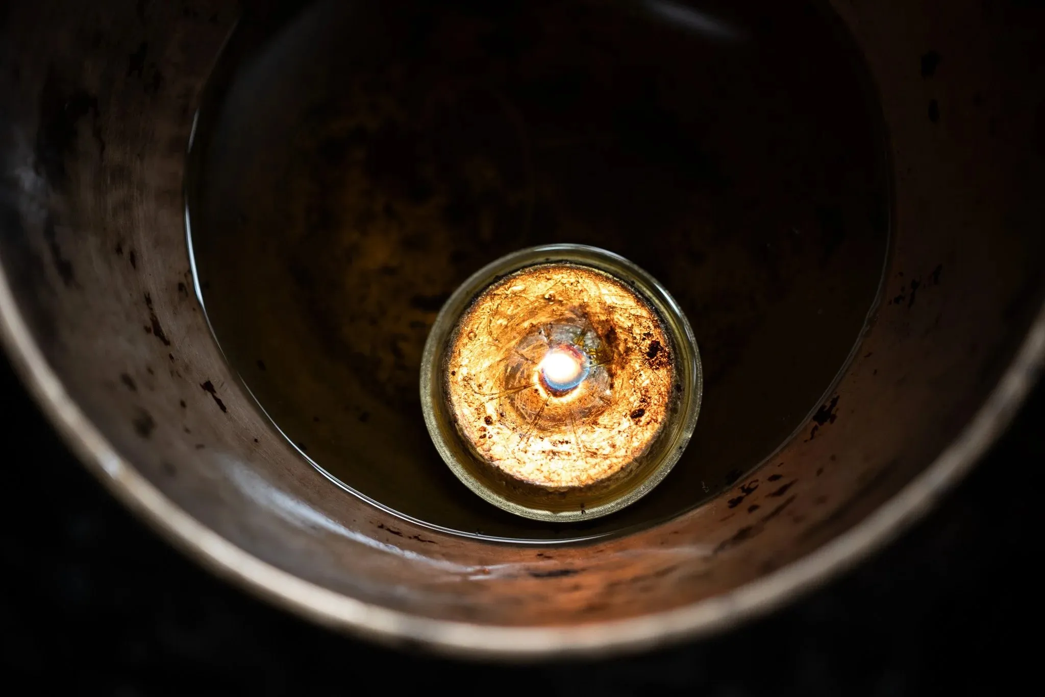 A single butter lamp glowing at the bottom of a metal holder