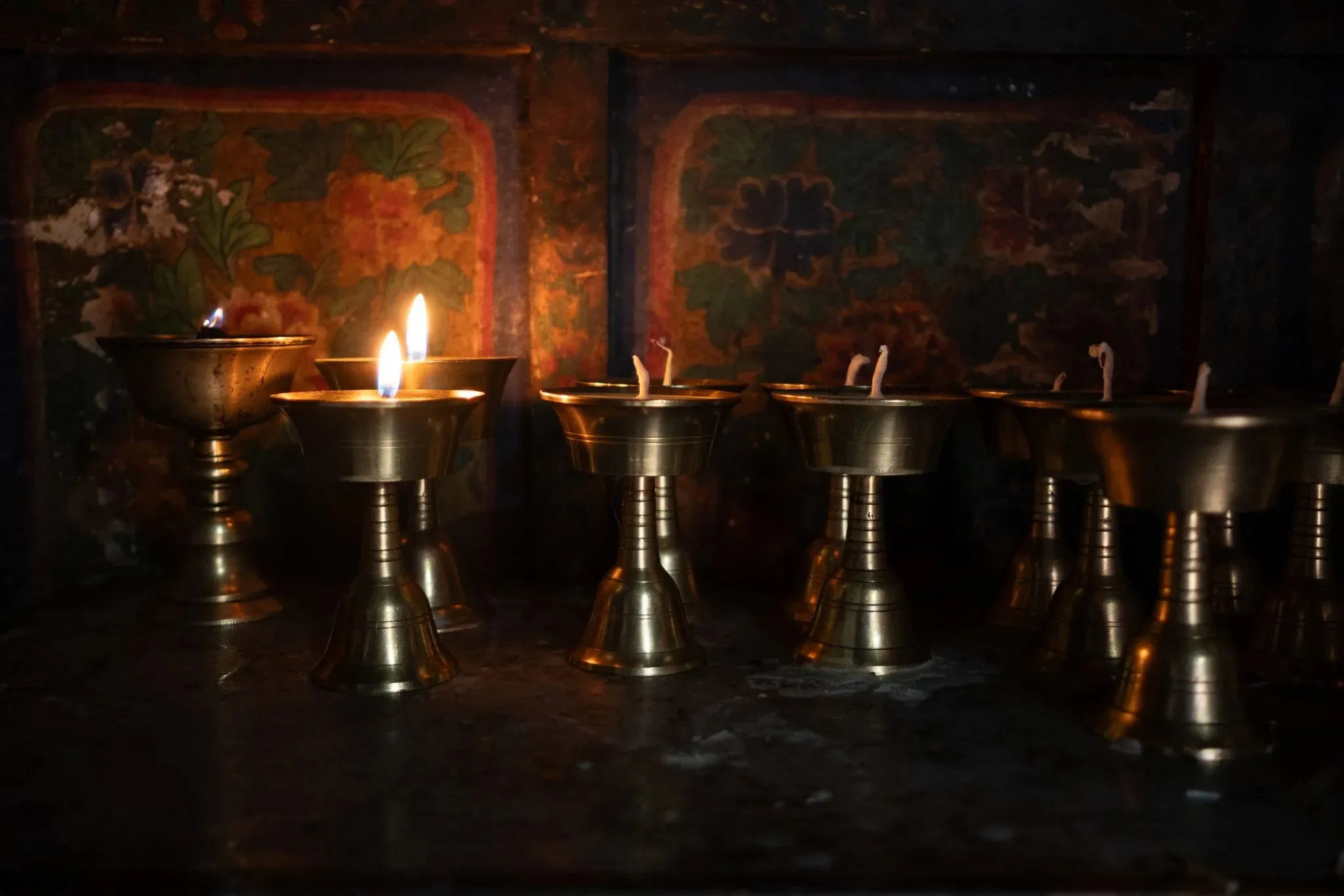 Butter lamps burning in front of painted walls inside the monastery