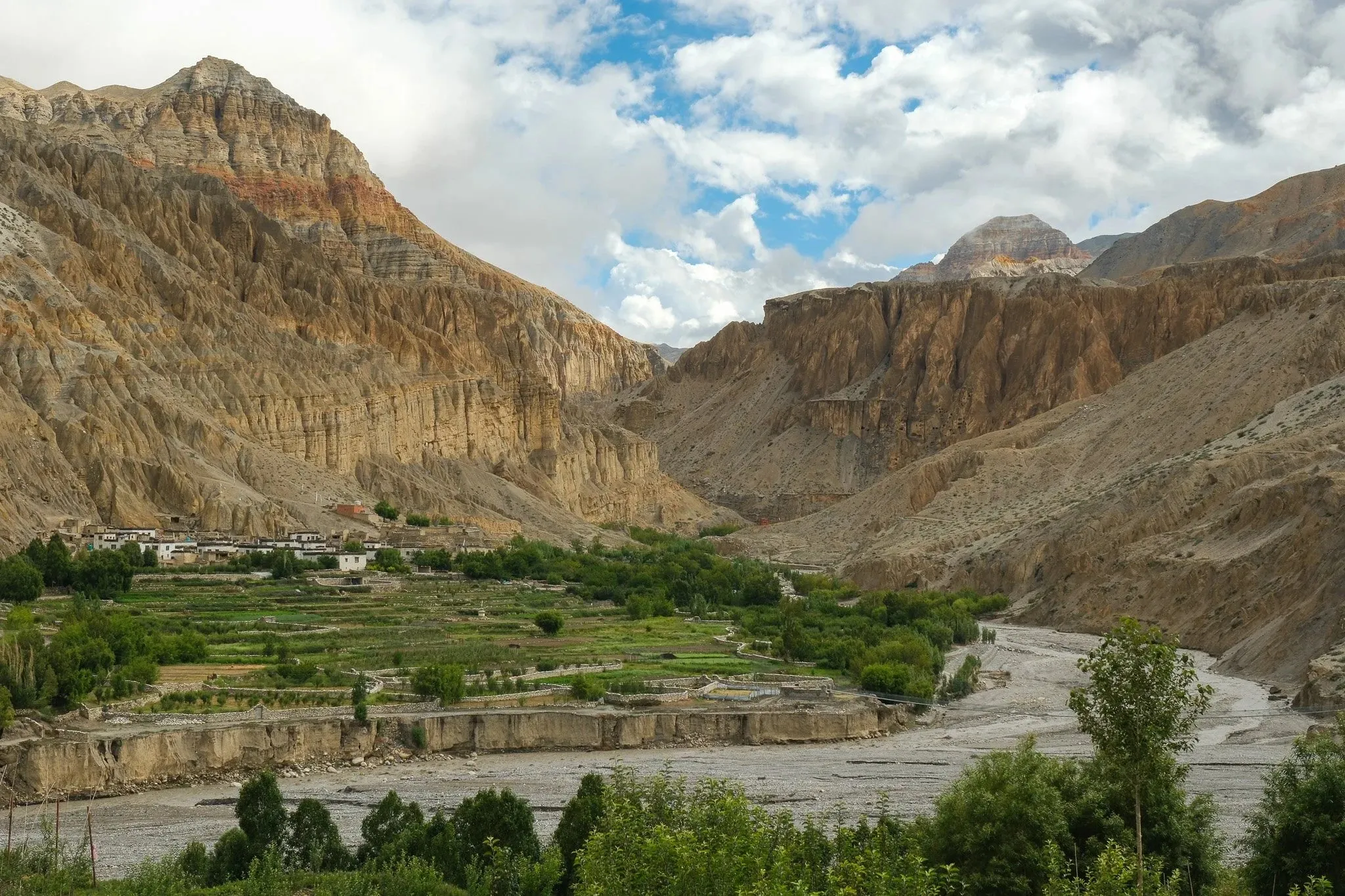 A green valley with fields and a river below red and ochre cliffs near Luri Gompa