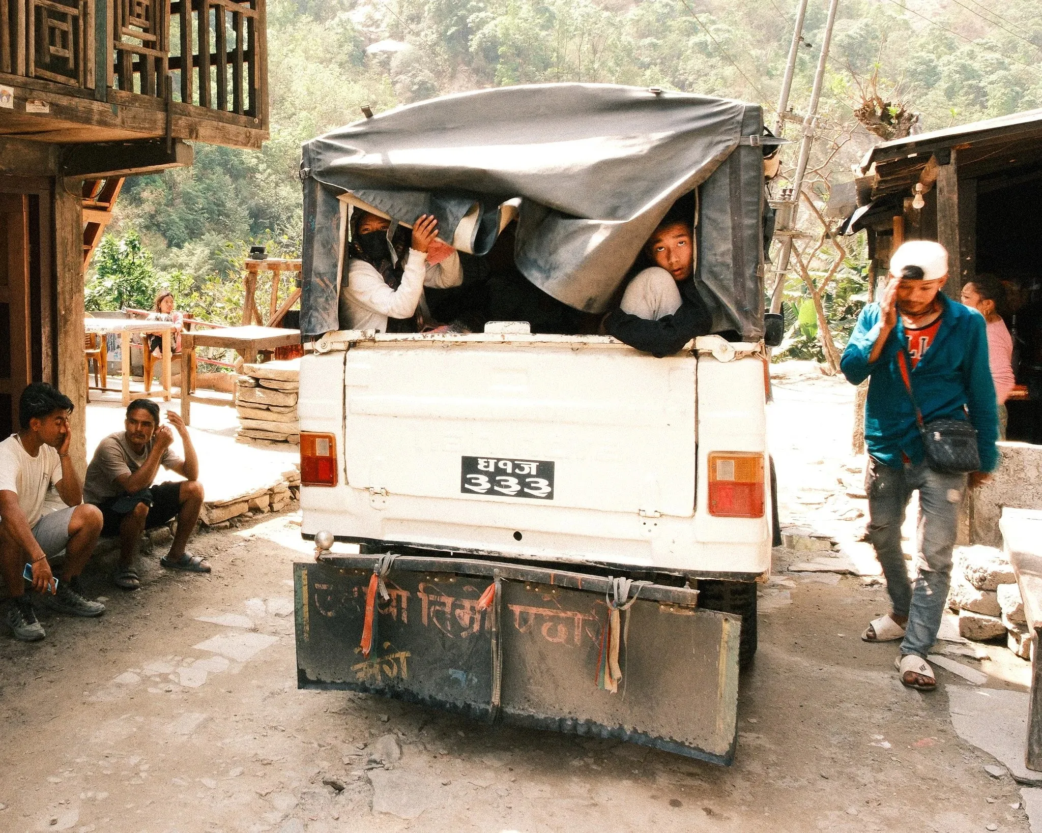 Passengers looking out of the back of a covered jeep in a village on the Manaslu road