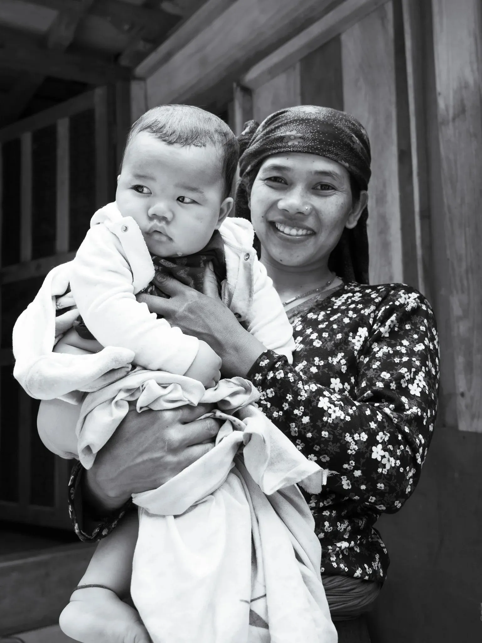 Black and white photo of a smiling woman holding a baby in a doorway