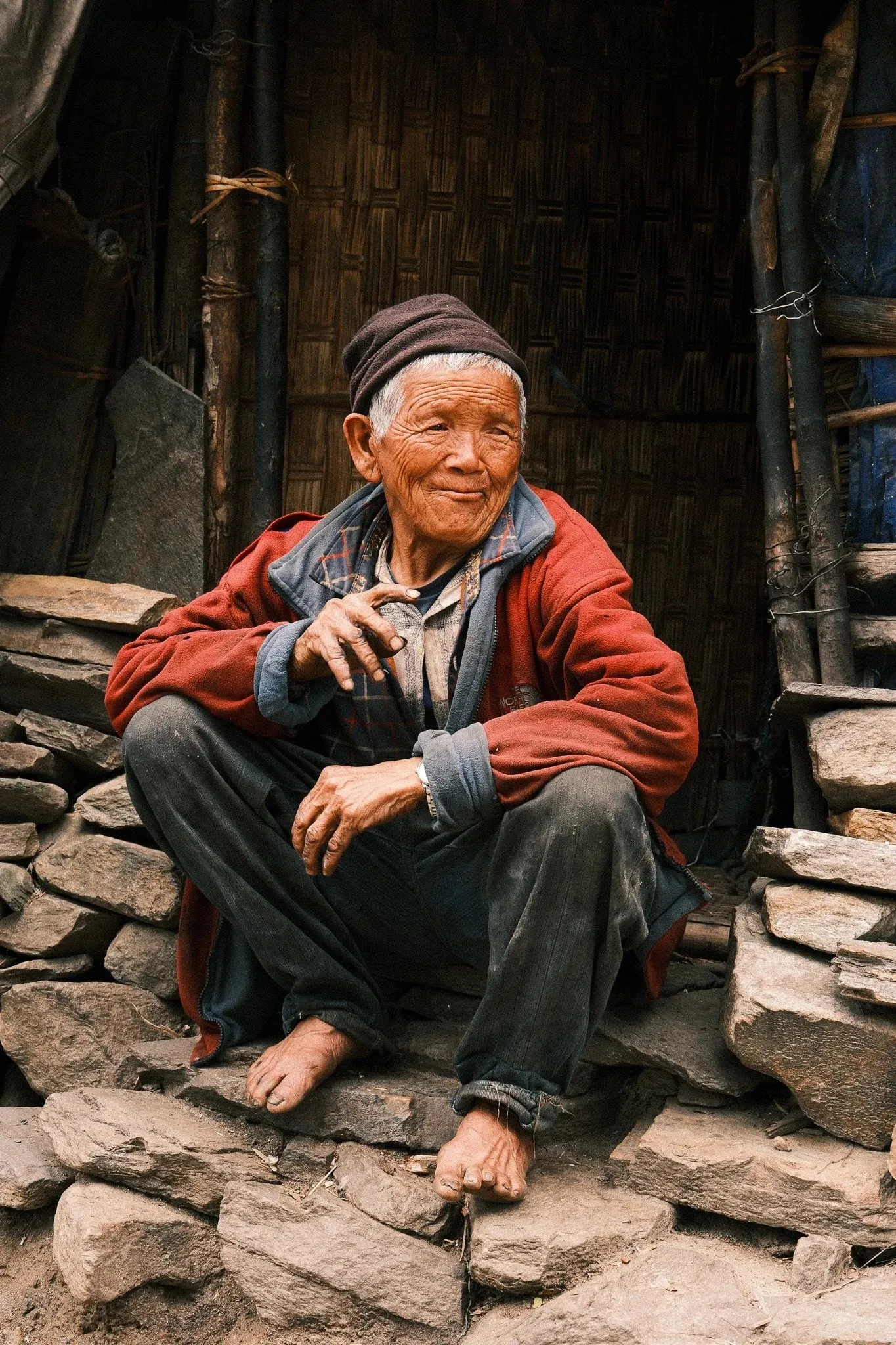 An older man in a red jacket sitting on stone steps in a doorway