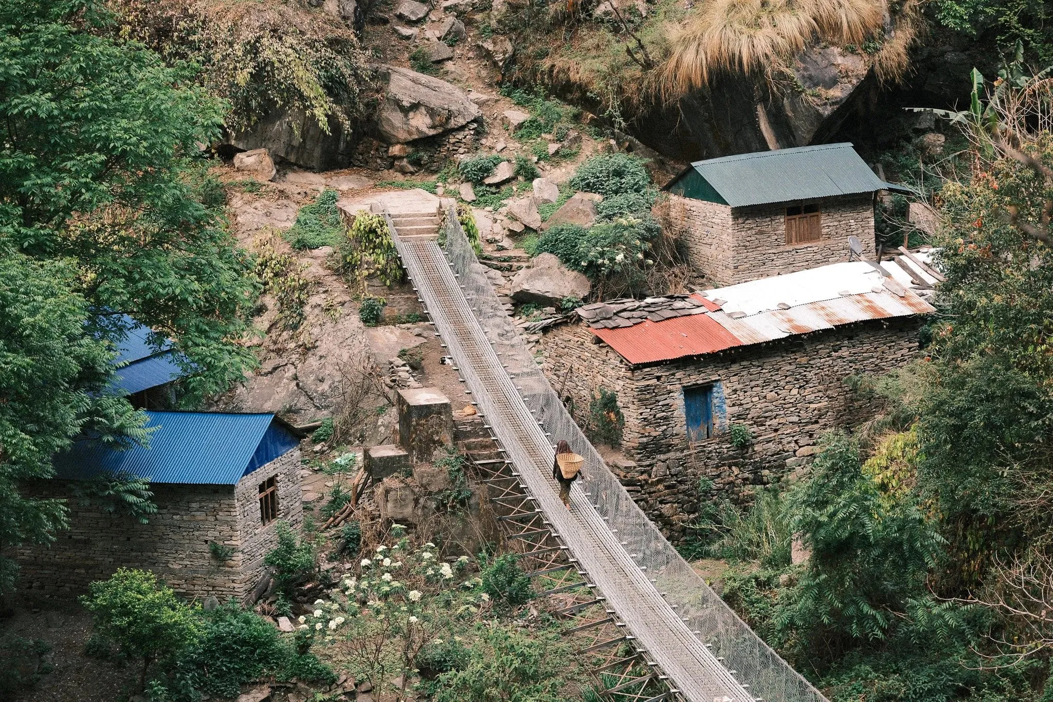 A suspension bridge leading to stone houses with coloured roofs in a green valley