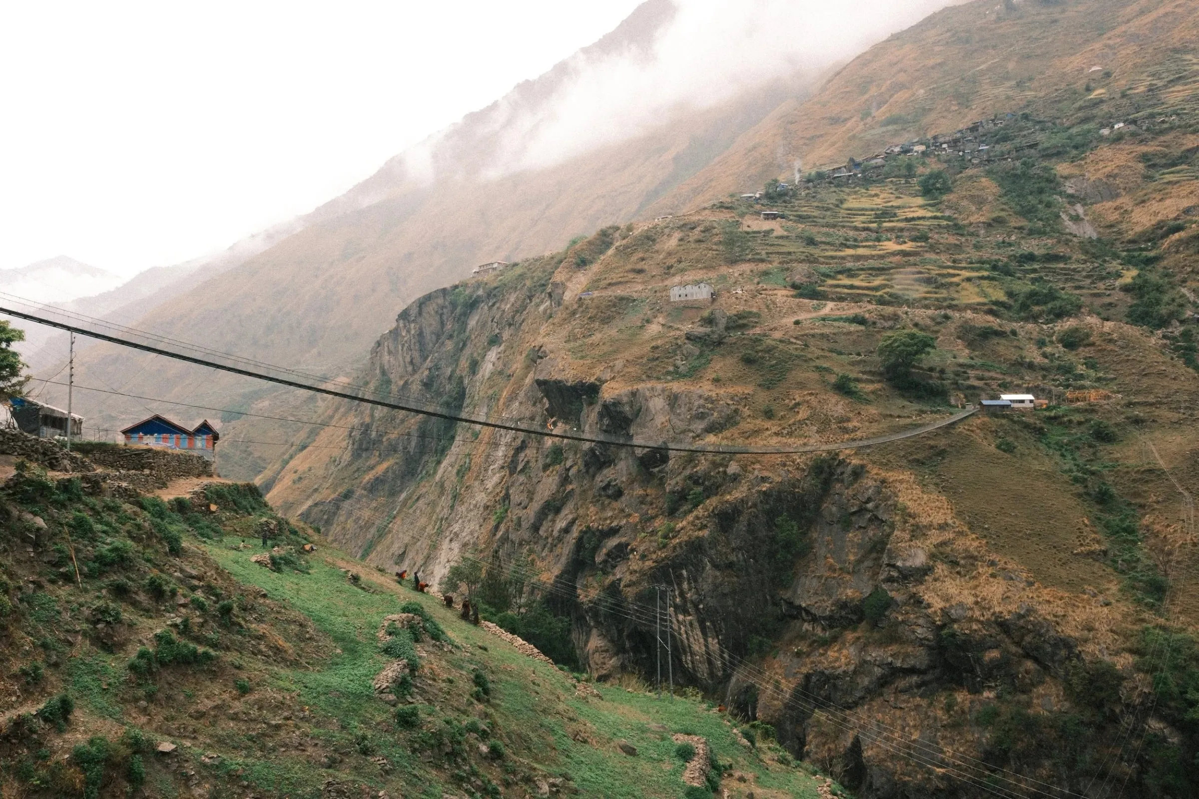 Terraced slopes and a deep river valley under low cloud on the Manaslu Circuit