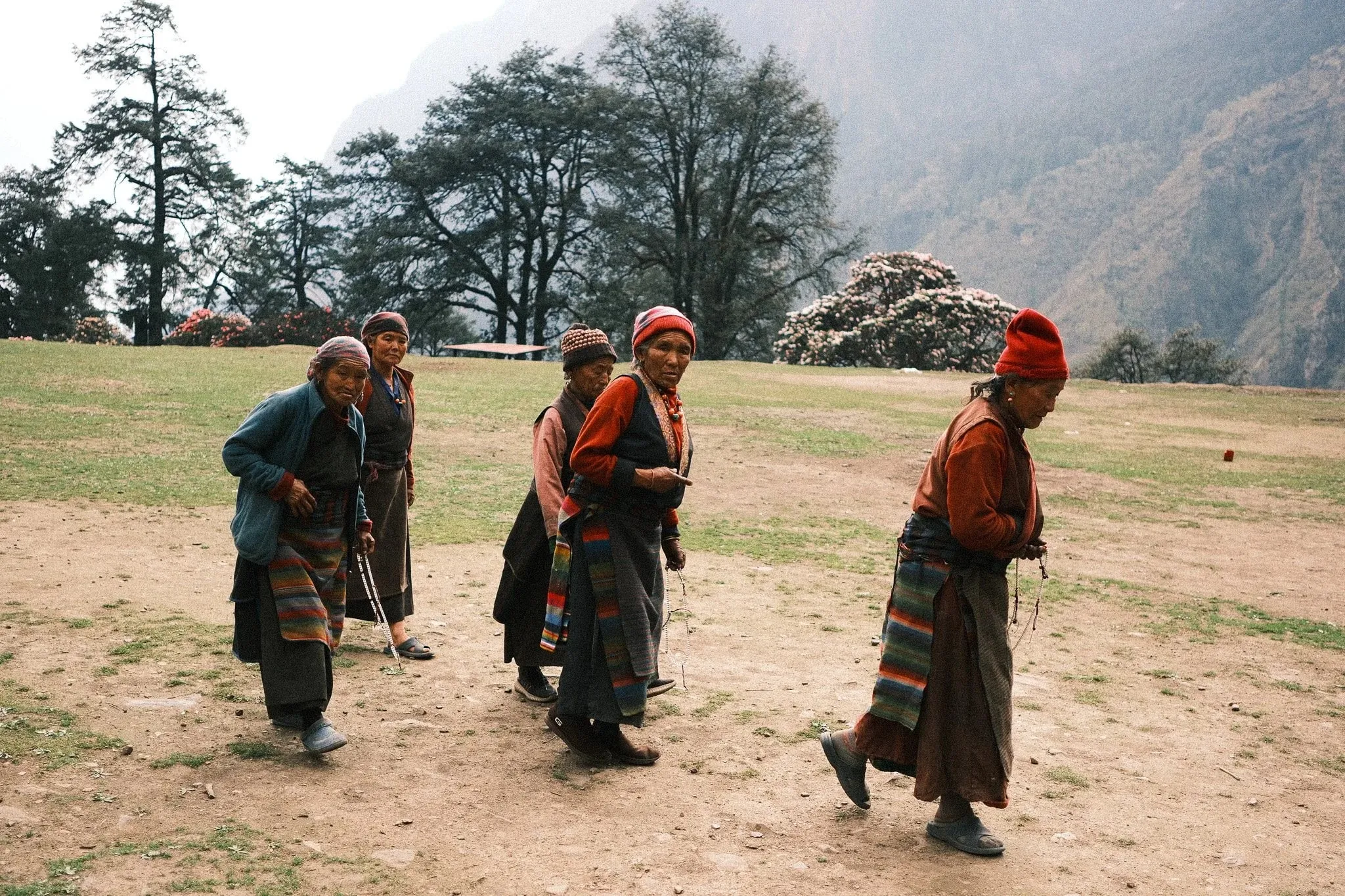 Women in traditional striped aprons walking across a grassy field below the mountains