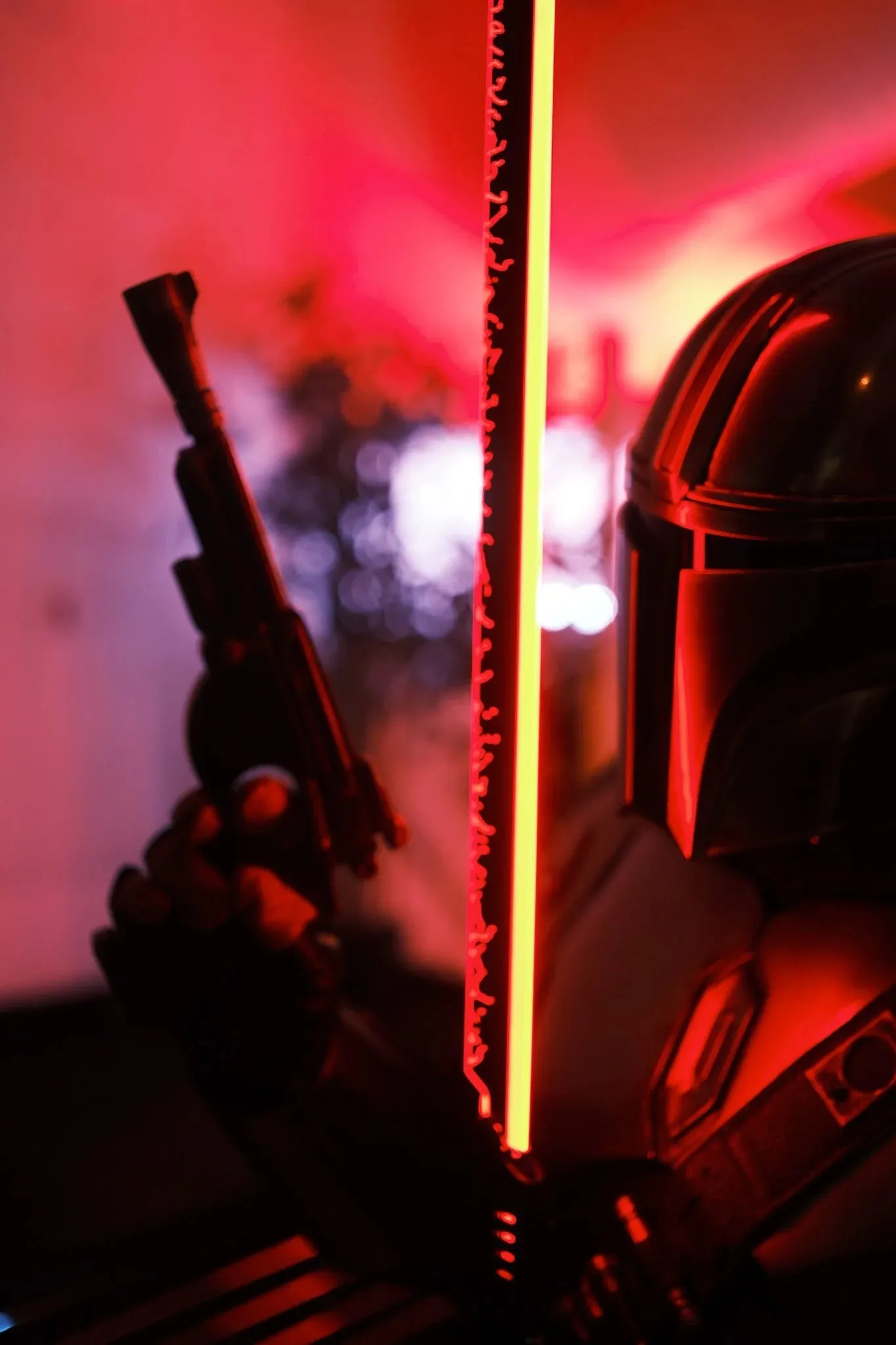 A cosplayer in a Mandalorian-style helmet holding a blaster beside a glowing light