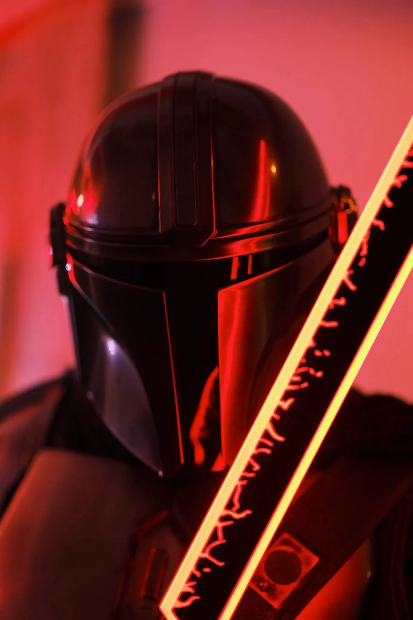 A cosplayer in a Mandalorian-style helmet holding a glowing sword under red light