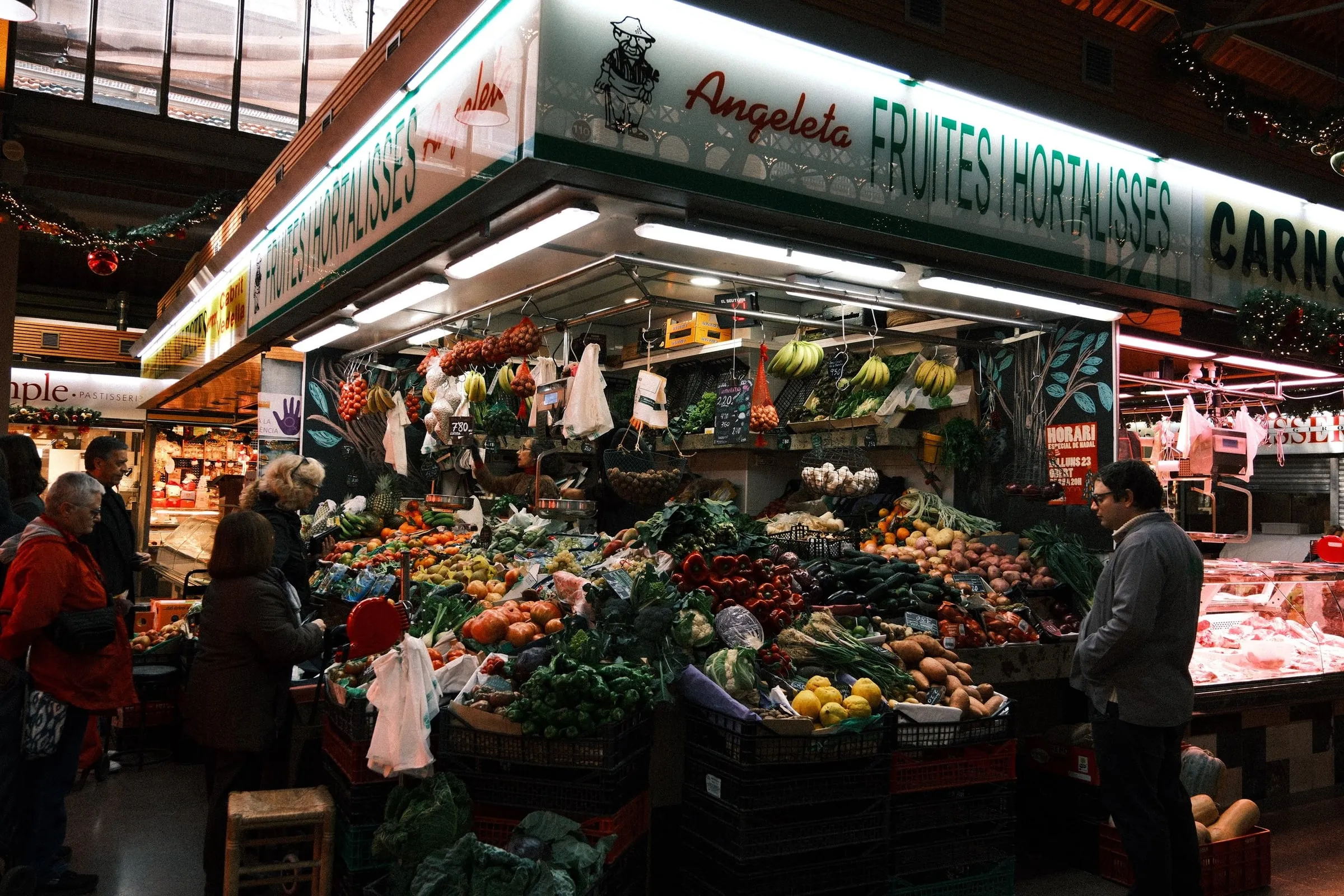 Shoppers at a brightly lit fruit and vegetable stall in a Barcelona market