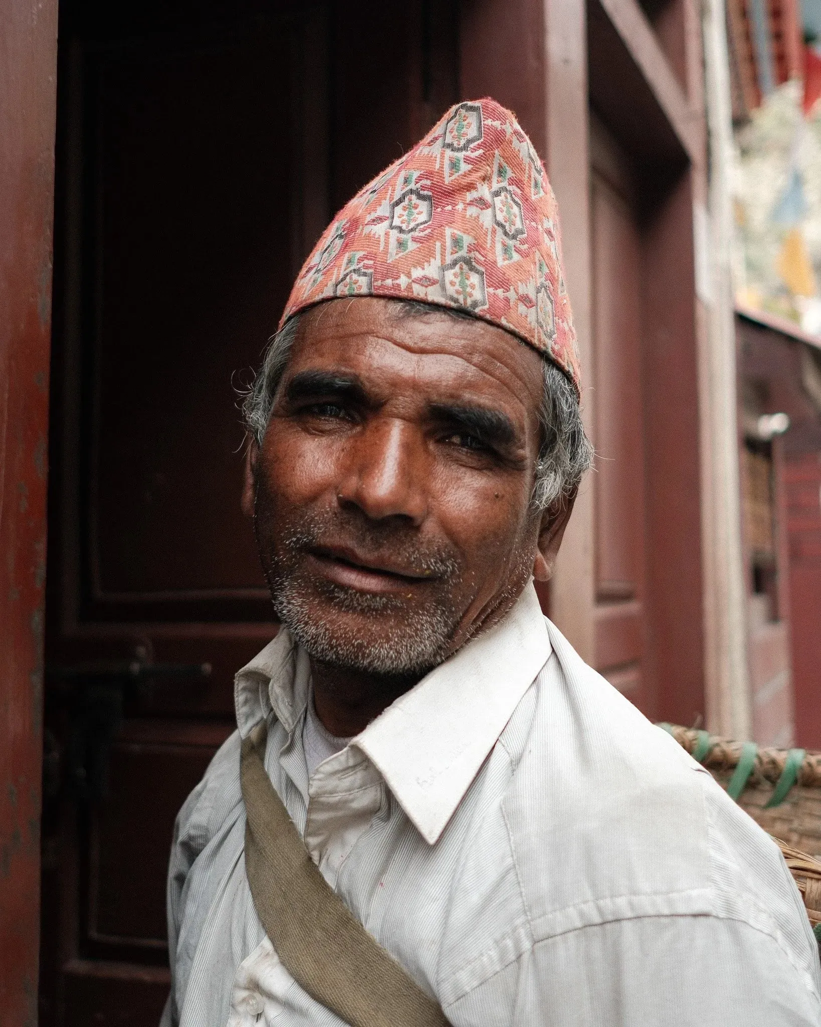 A smiling older man in a dhaka topi in a doorway in Marpha