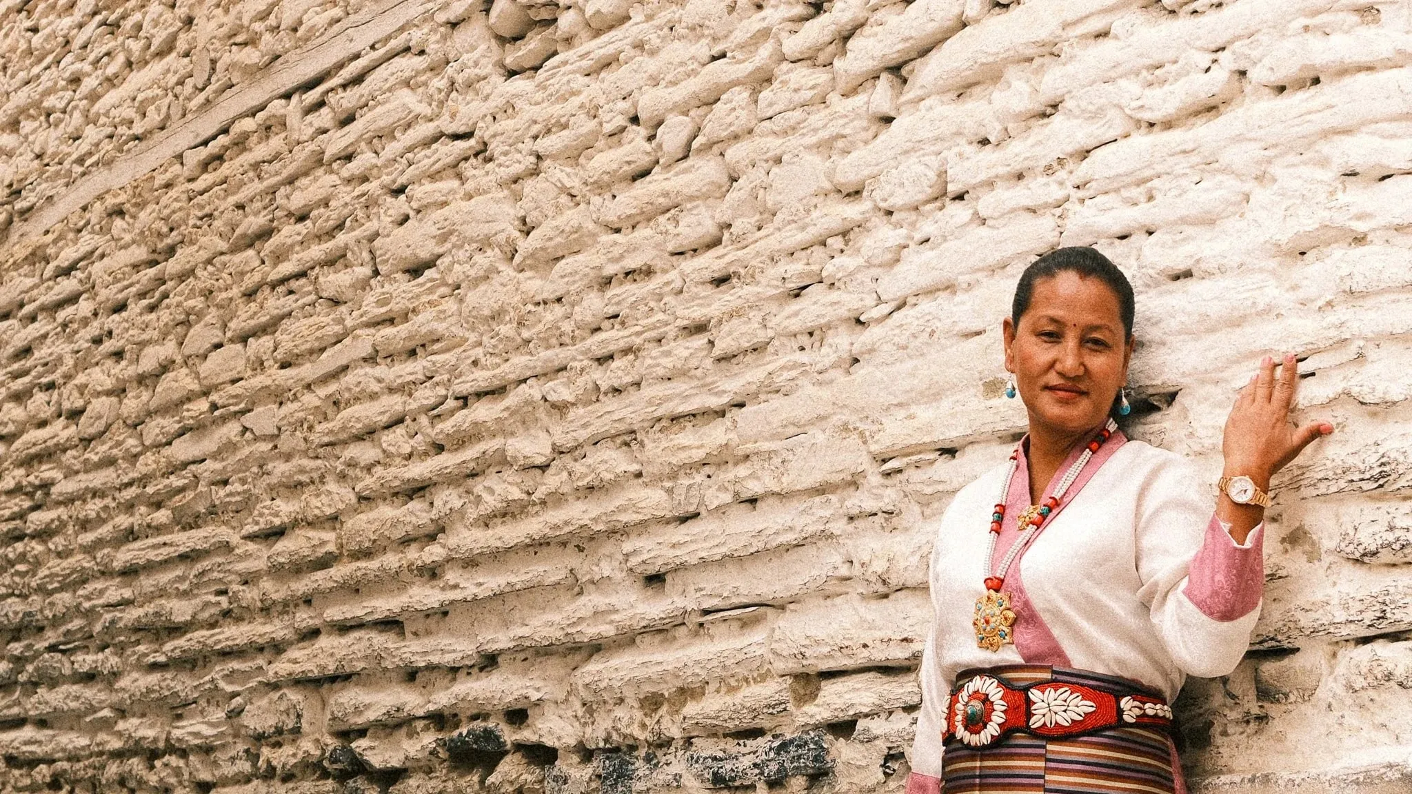 A woman in traditional dress and jewellery standing against a whitewashed wall in Marpha