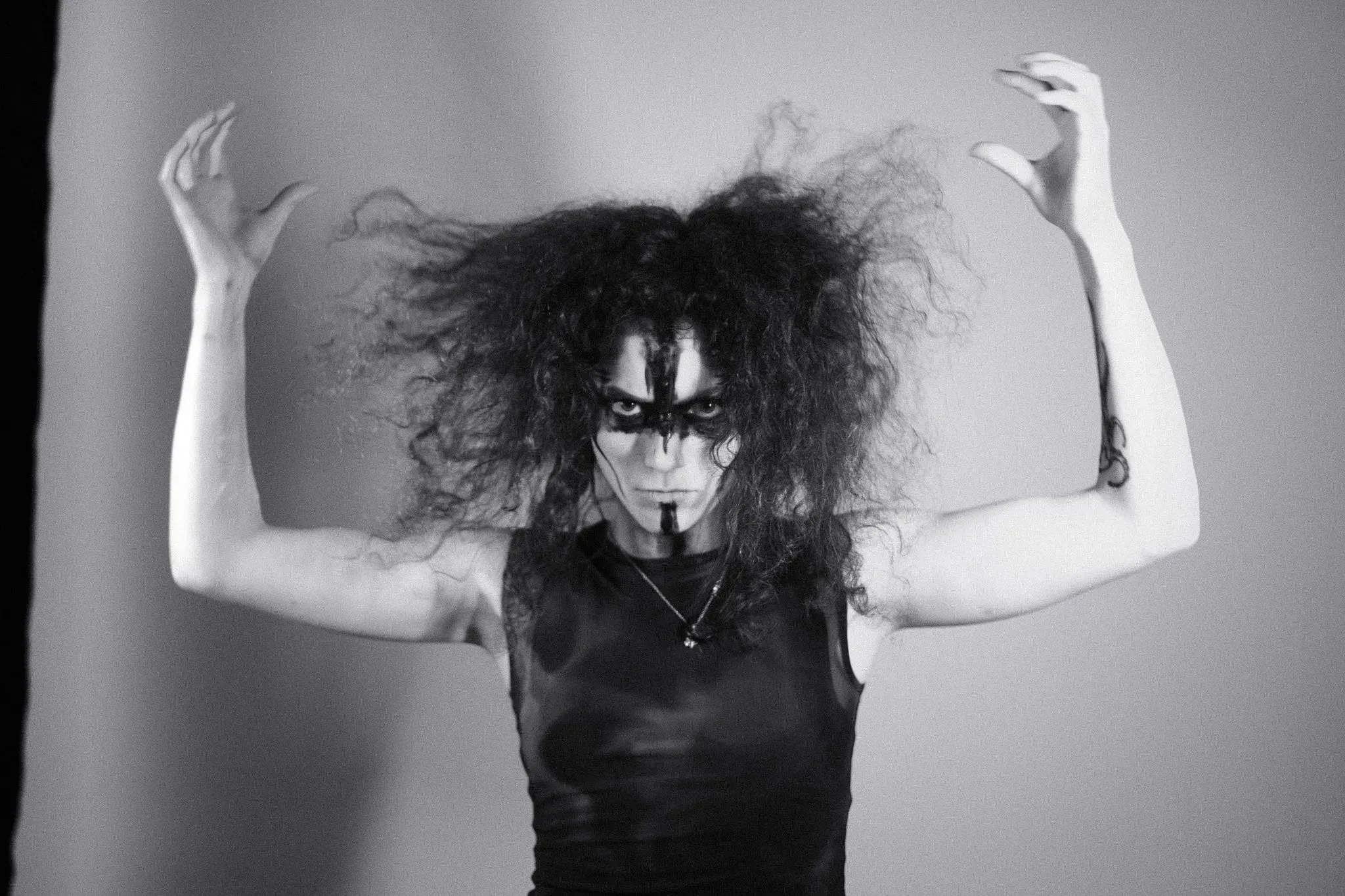 Black and white photo of a model in face paint with arms raised and hair spread wide