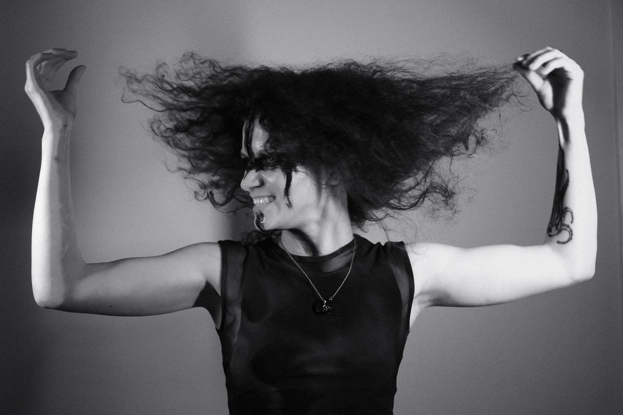 Black and white photo of a model with face paint lifting her curly hair with both hands