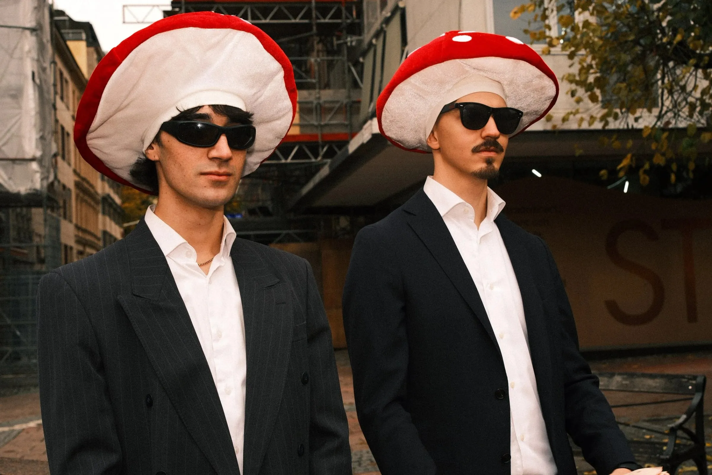 Two men in suits, sunglasses and red and white mushroom hats