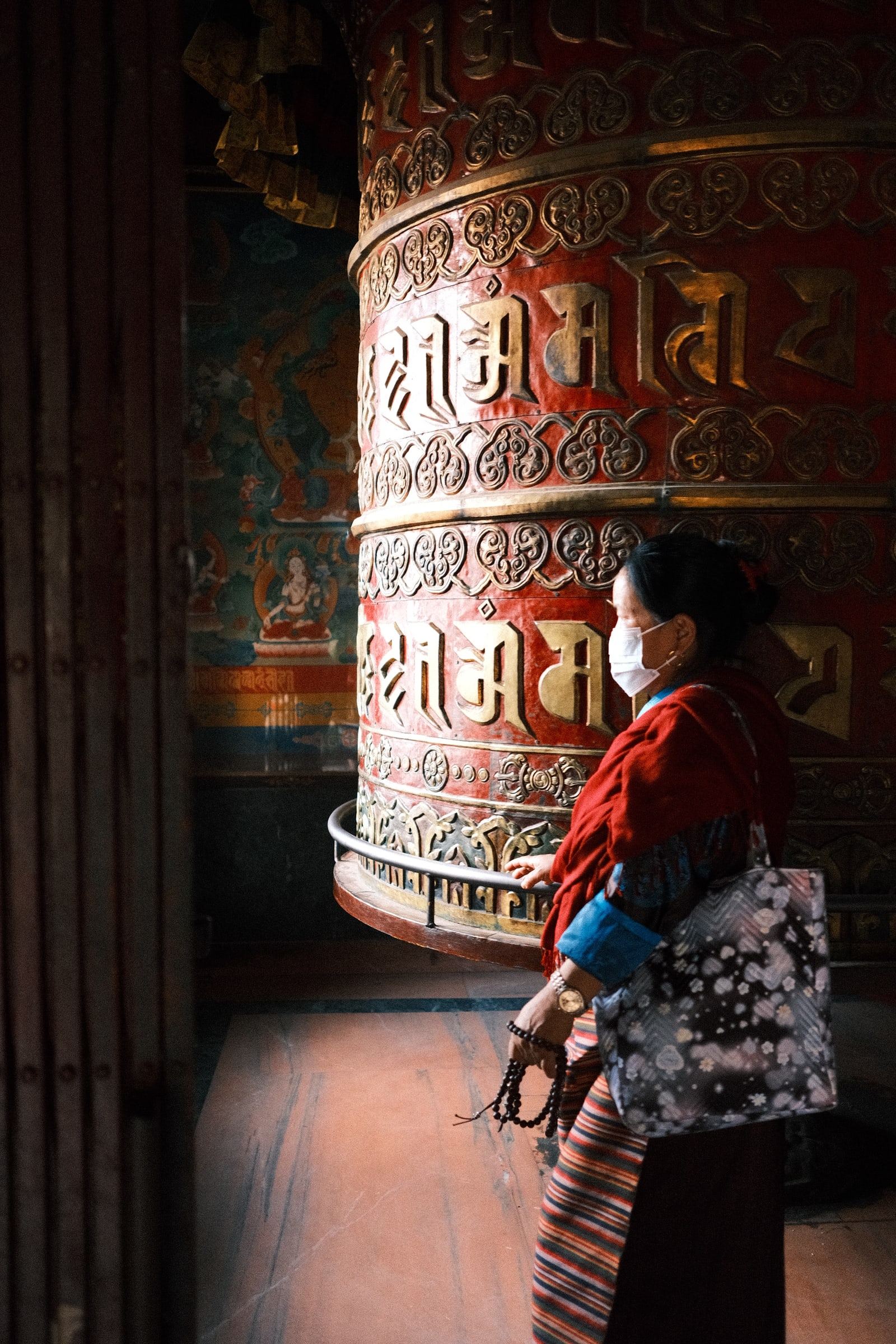Woman in a face mask walking past a large red prayer wheel