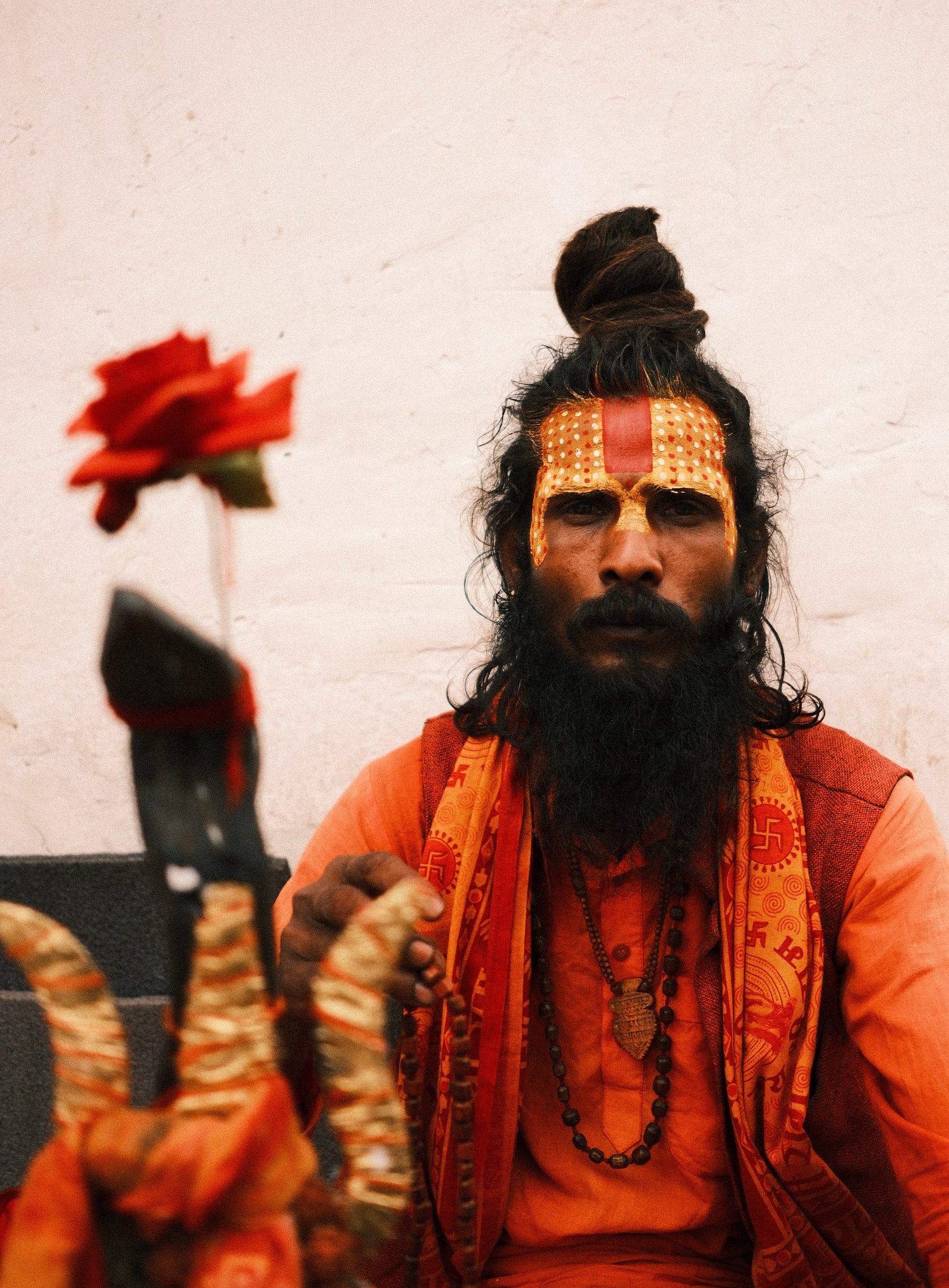 Sadhu with a painted forehead and orange robes, seated beside a red flower