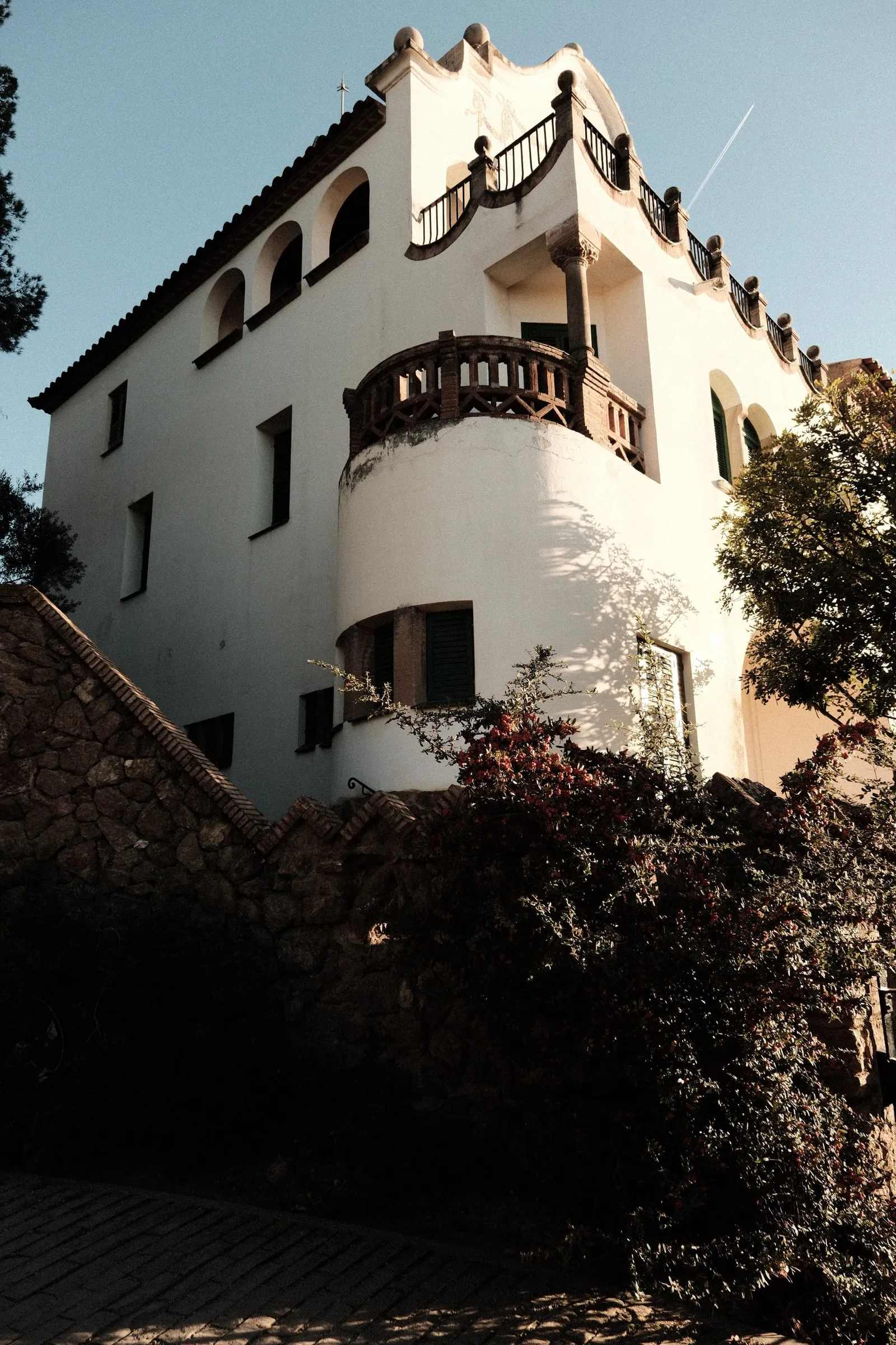 A white house with rounded balconies above a stone wall in Park Güell