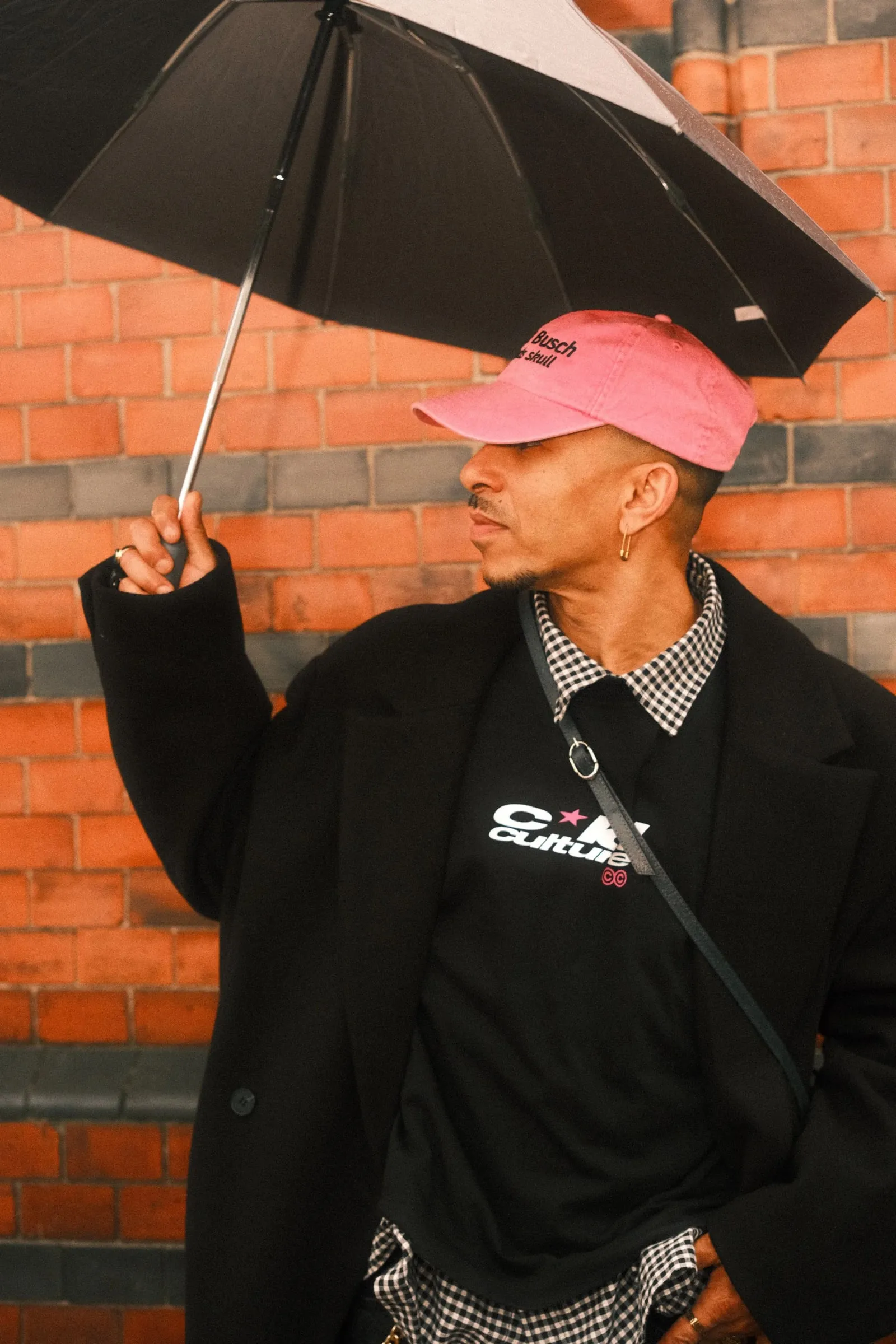 A man in a pink cap and black coat holding an umbrella, looking to the side