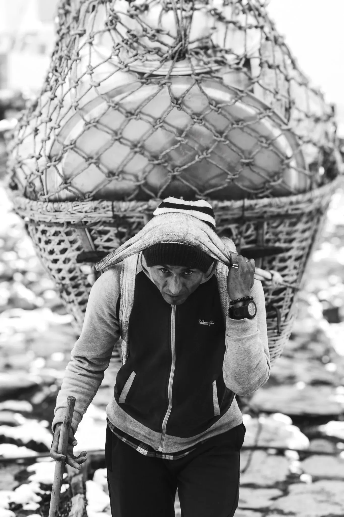 Black and white photo of a porter carrying a large netted basket with a head strap