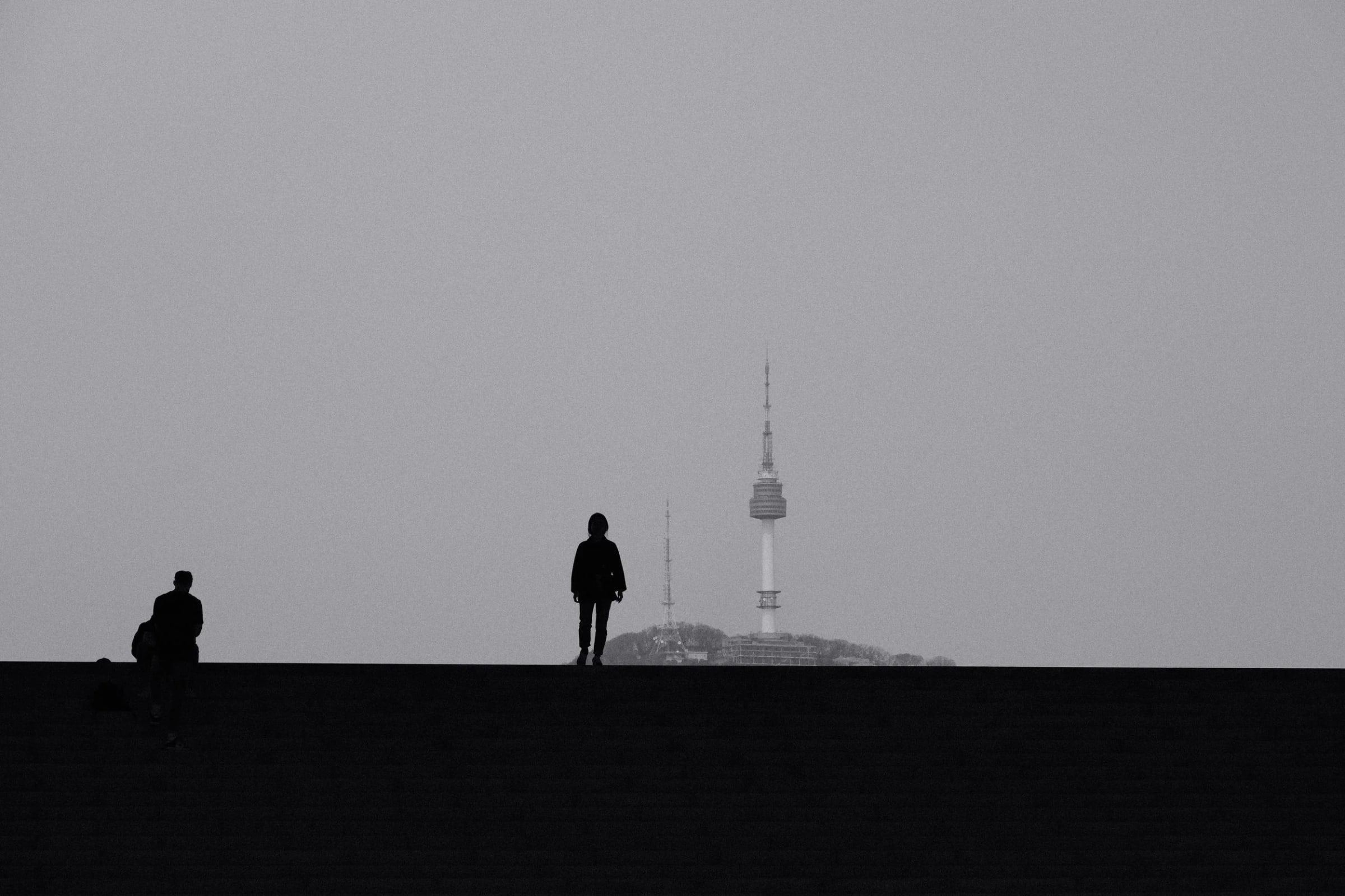 Two silhouetted figures on a ridge, with N Seoul Tower on the hill behind