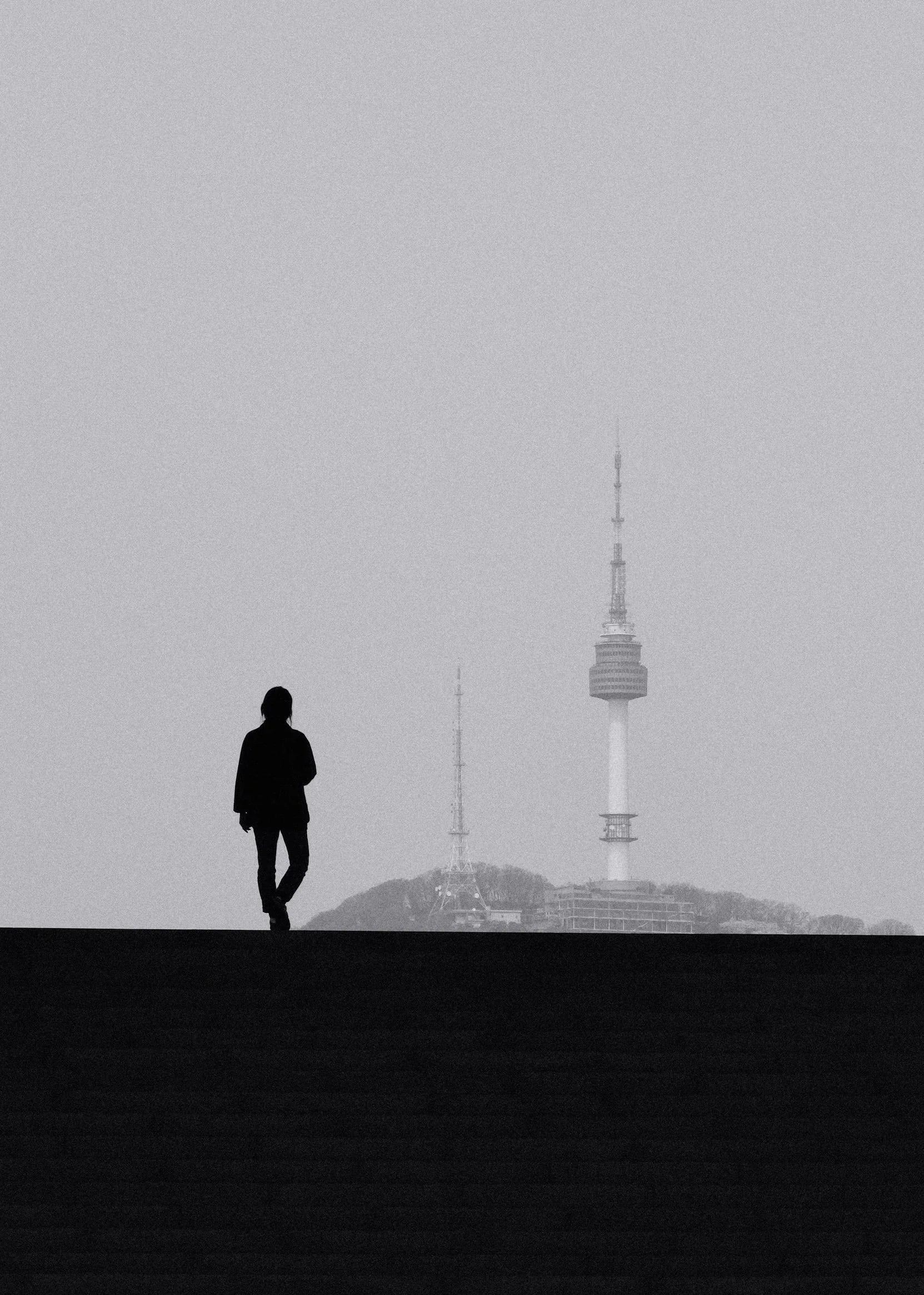 Lone figure walking along a ridge, with N Seoul Tower in the distance