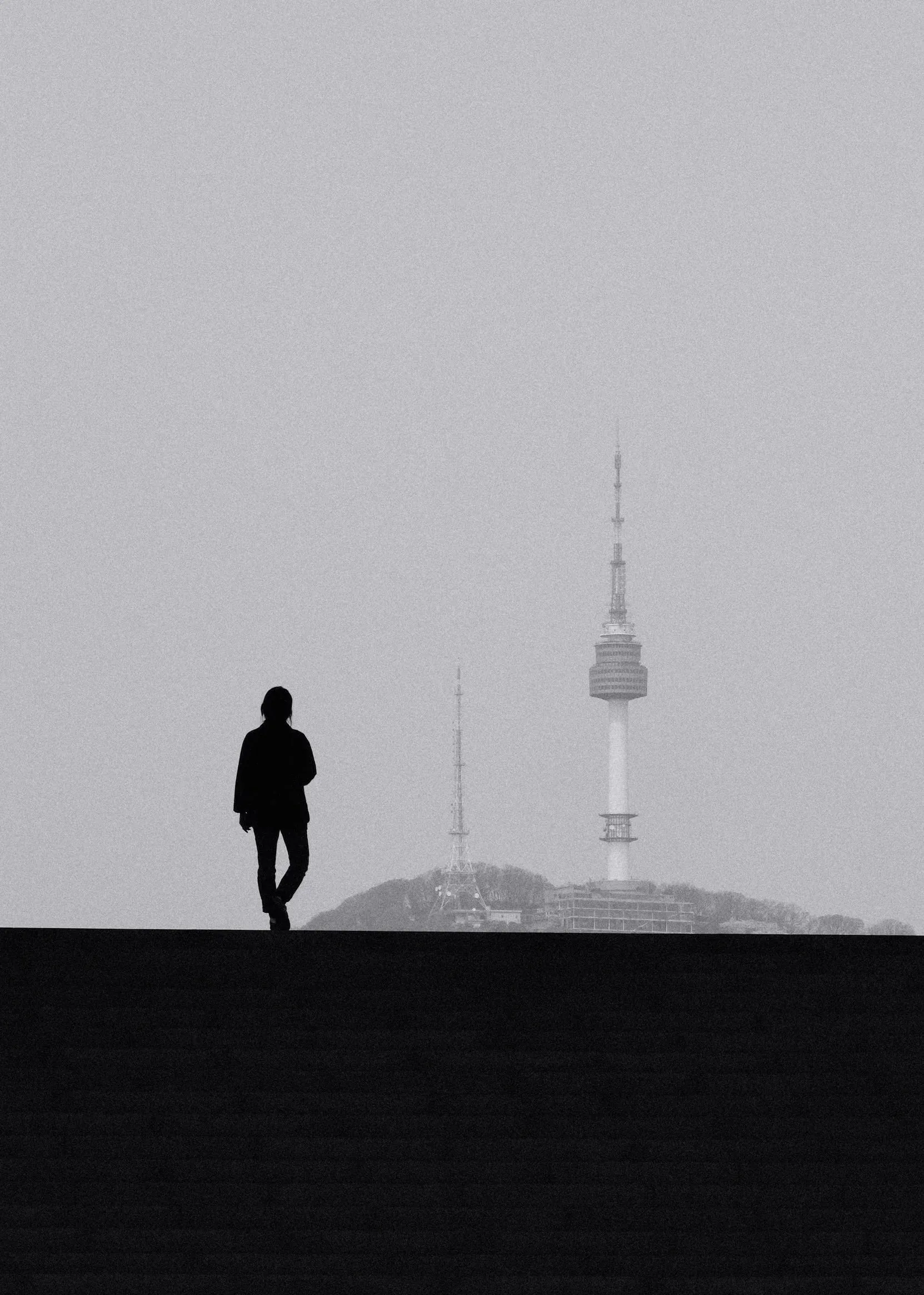 A figure in silhouette on the steps of the National Museum of Korea, with Namsan Tower in the haze behind