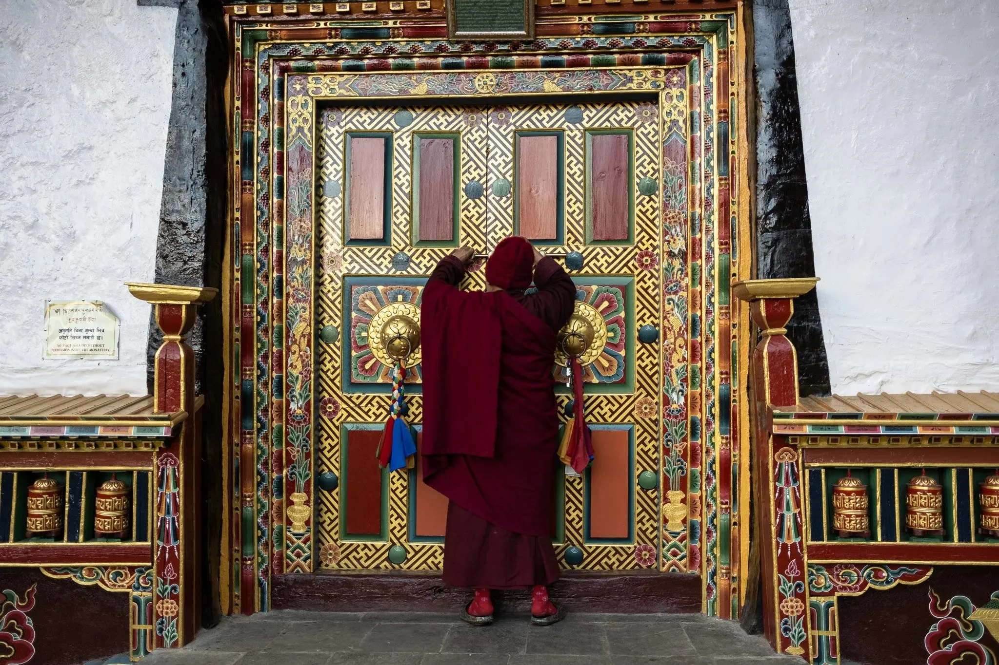A monk opening an ornate painted door at Serang Monastery