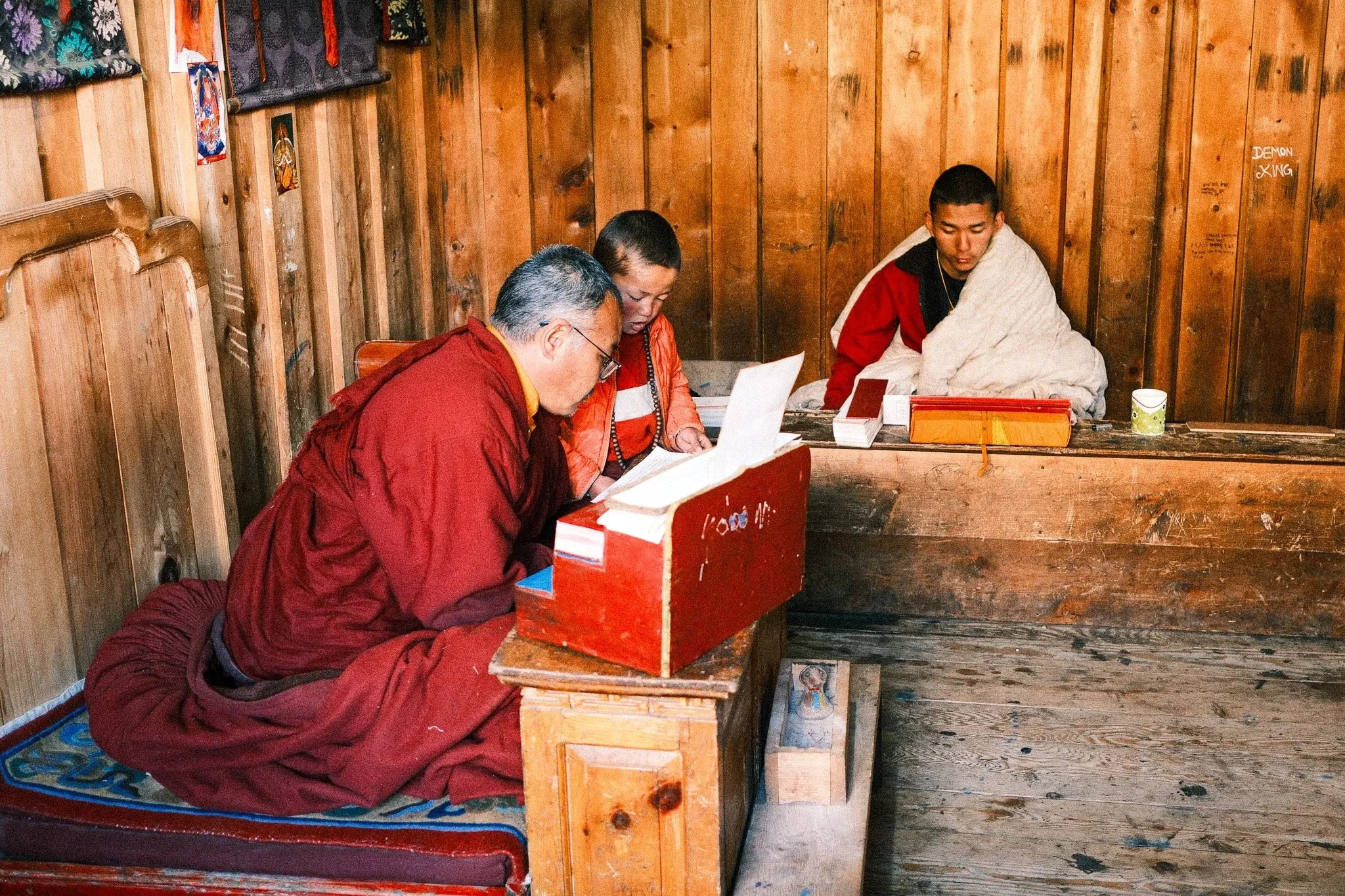 Monks in maroon robes reading texts at low wooden tables at Serang Monastery