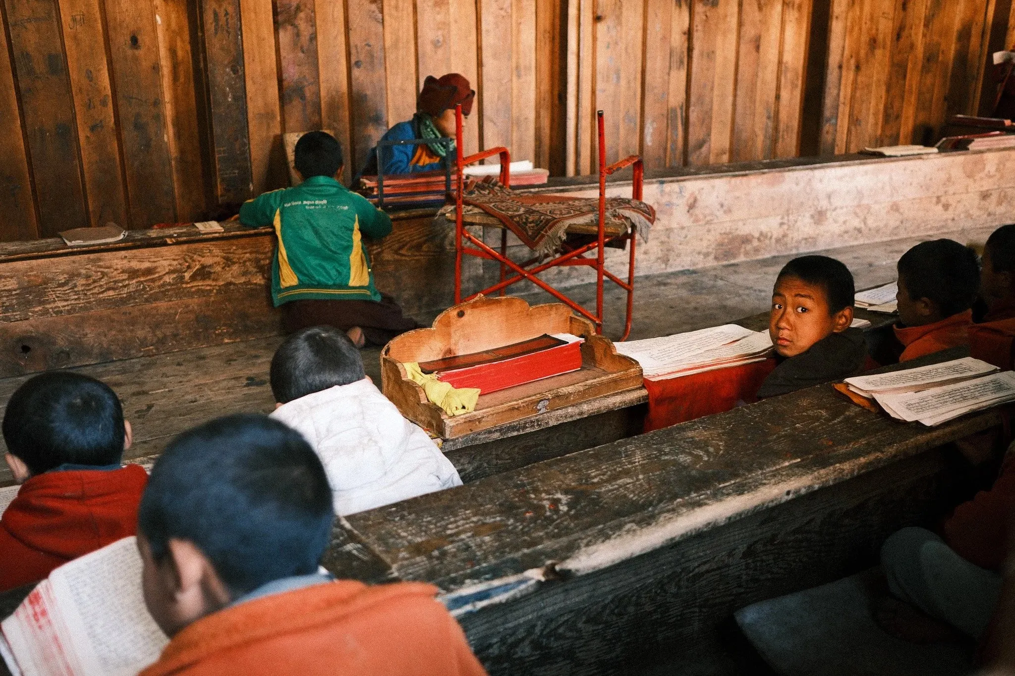 Young monks reading at long wooden desks in a classroom at Serang Monastery