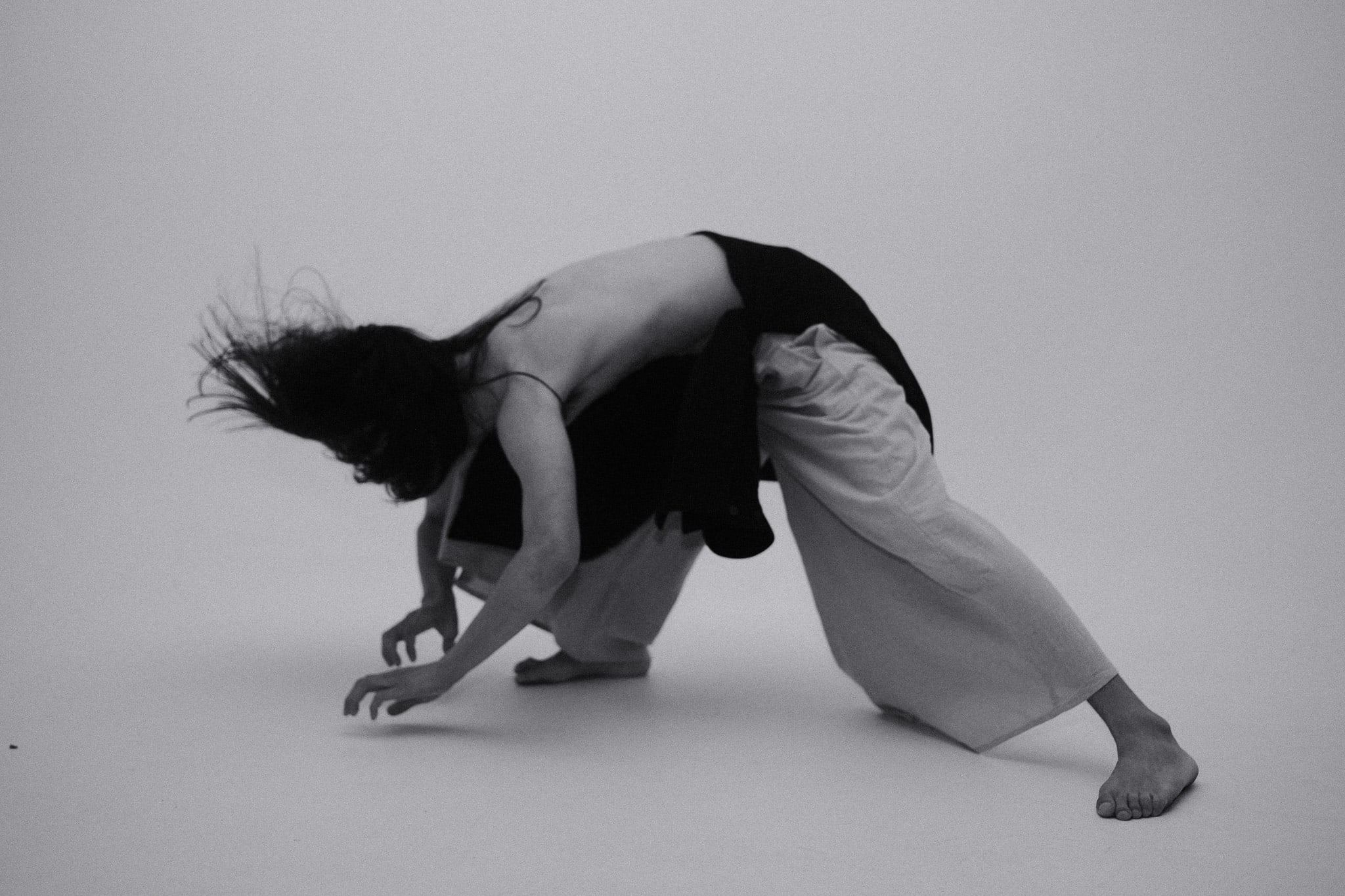 Black-and-white image of a dancer bent low to the floor, hair flung outward