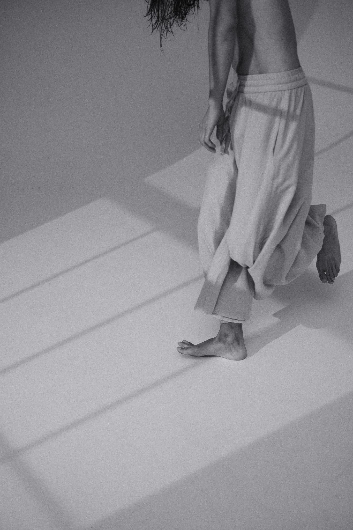 Black-and-white crop of a dancer's legs and loose trousers on a sunlit floor
