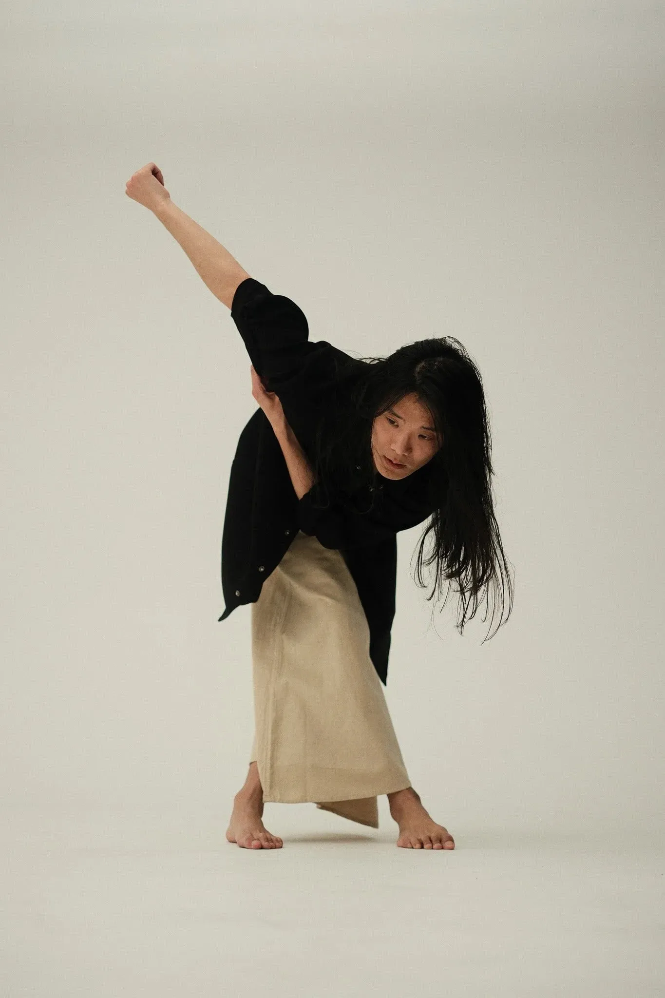 A model bending forward with one arm raised in a dance pose against a plain backdrop