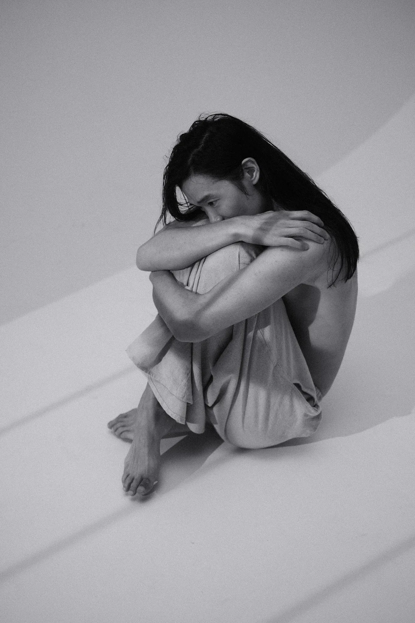 Black and white photo of a model sitting on the floor hugging their knees