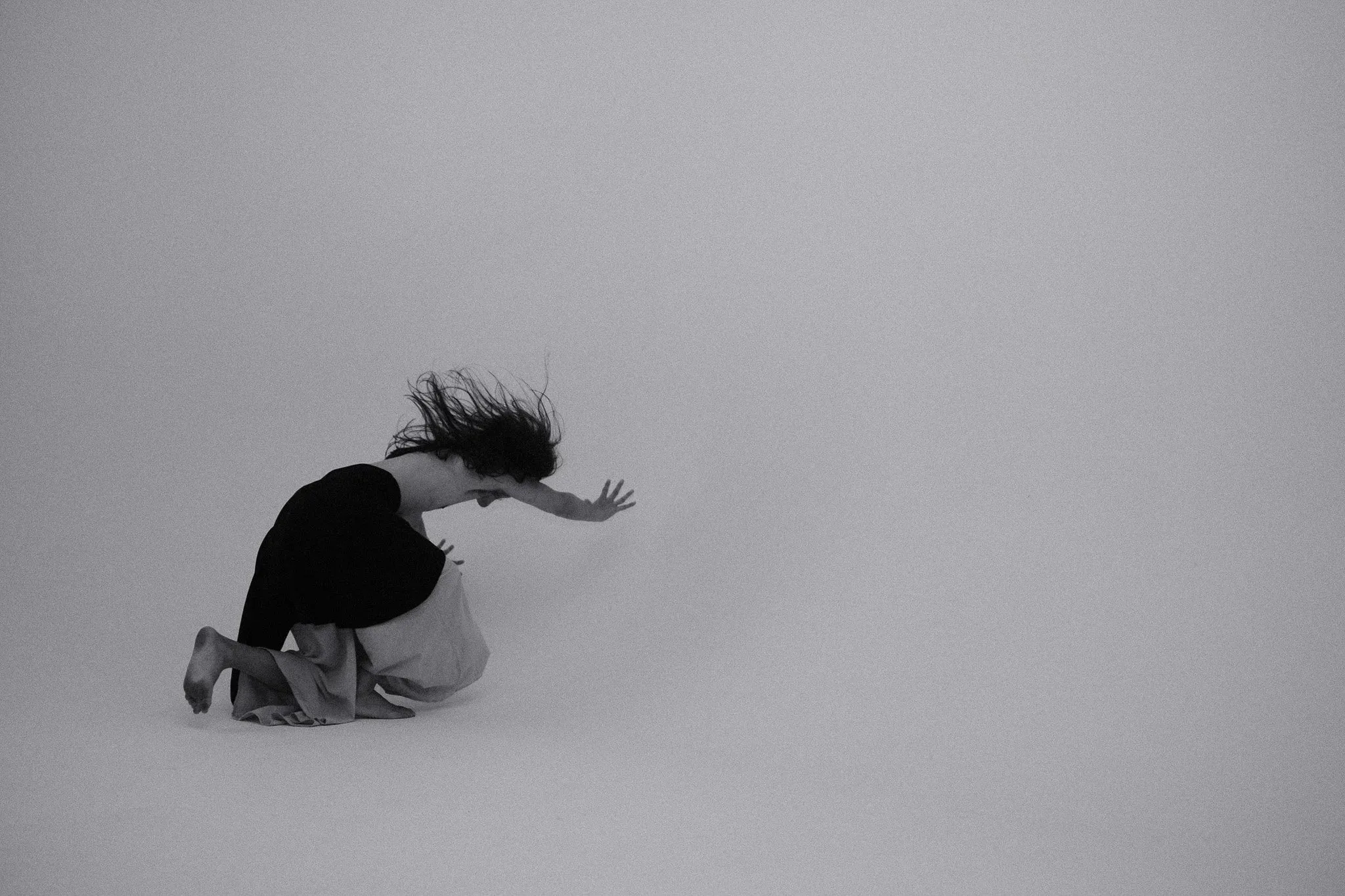A model kneeling and throwing their hair forward against a grey backdrop