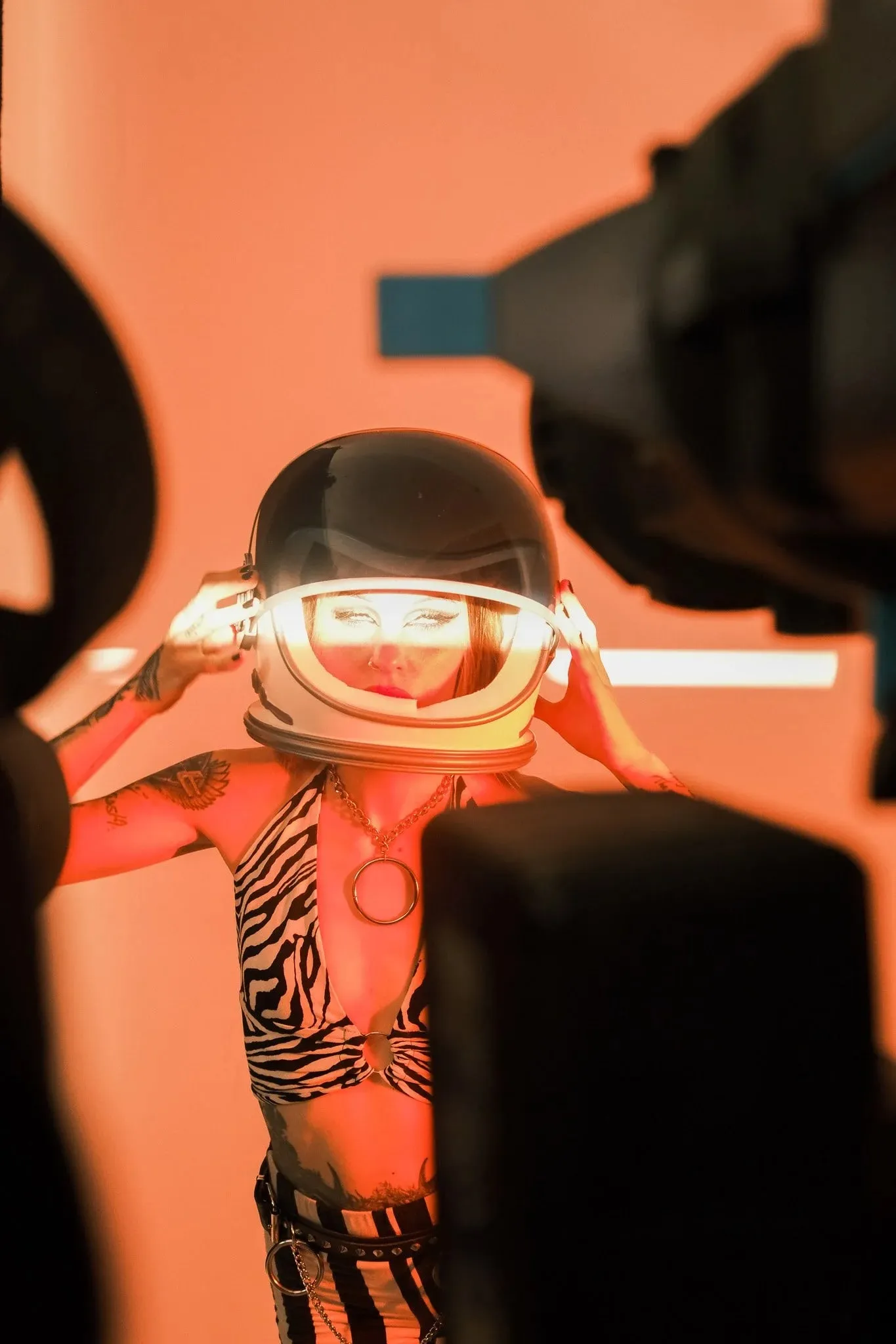A model in a glowing space helmet under orange light, framed by studio equipment